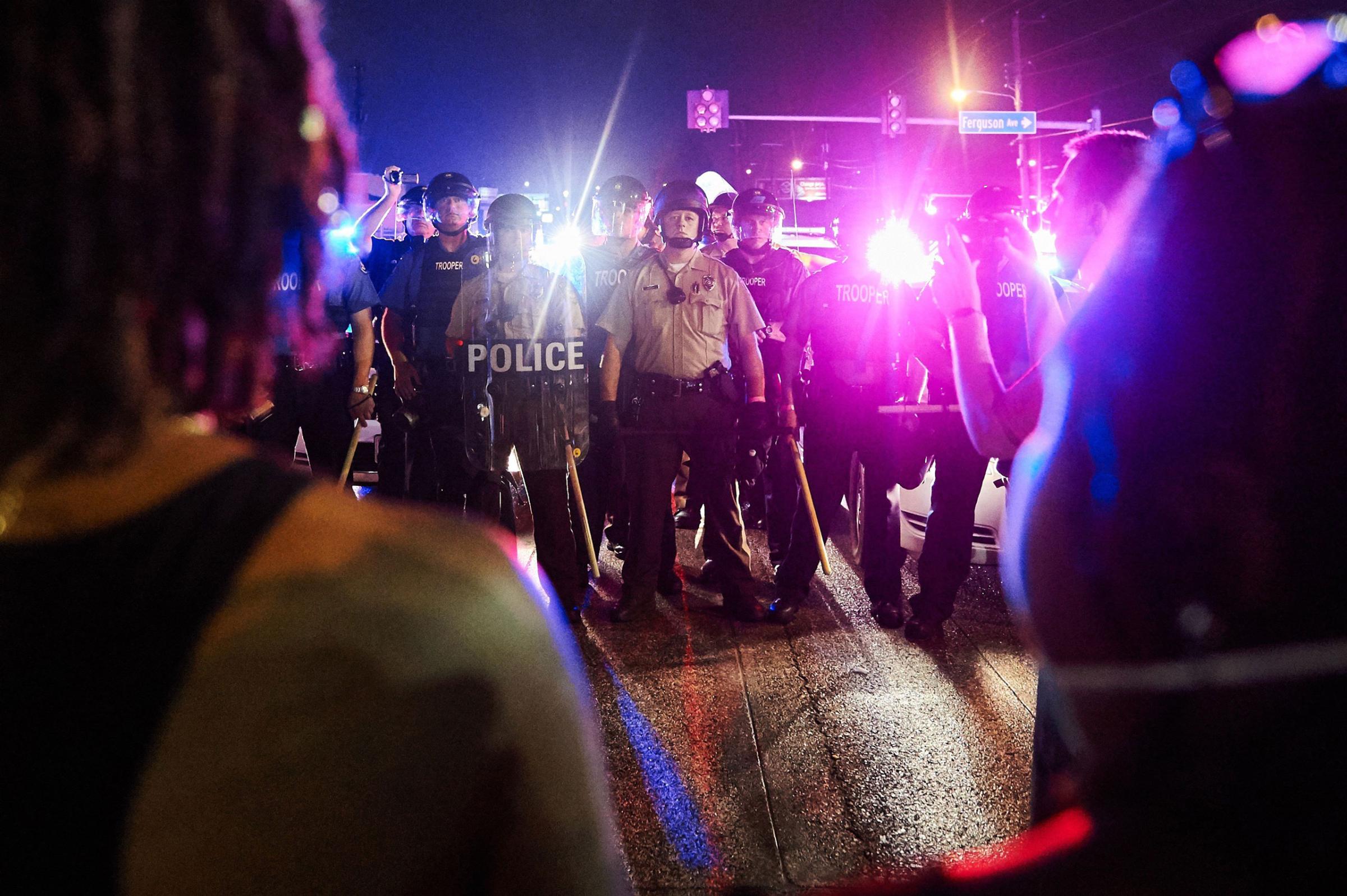 St. Louis County Police and Missouri State Highway Patrol troopers (C) stand guard as protesters (foreground) march on West Florissant Avenue in Ferguson, Missouri on August 9, 2015. A day of peaceful remembrance marking the anniversary of 18-year-old black teen Michael Brown's killing by police in the US city of Ferguson came to a violent end on August 9 as gunfire left at least one protester injured. AFP PHOTO / MICHAEL B. THOMASMichael B. Thomas/AFP/Getty Images