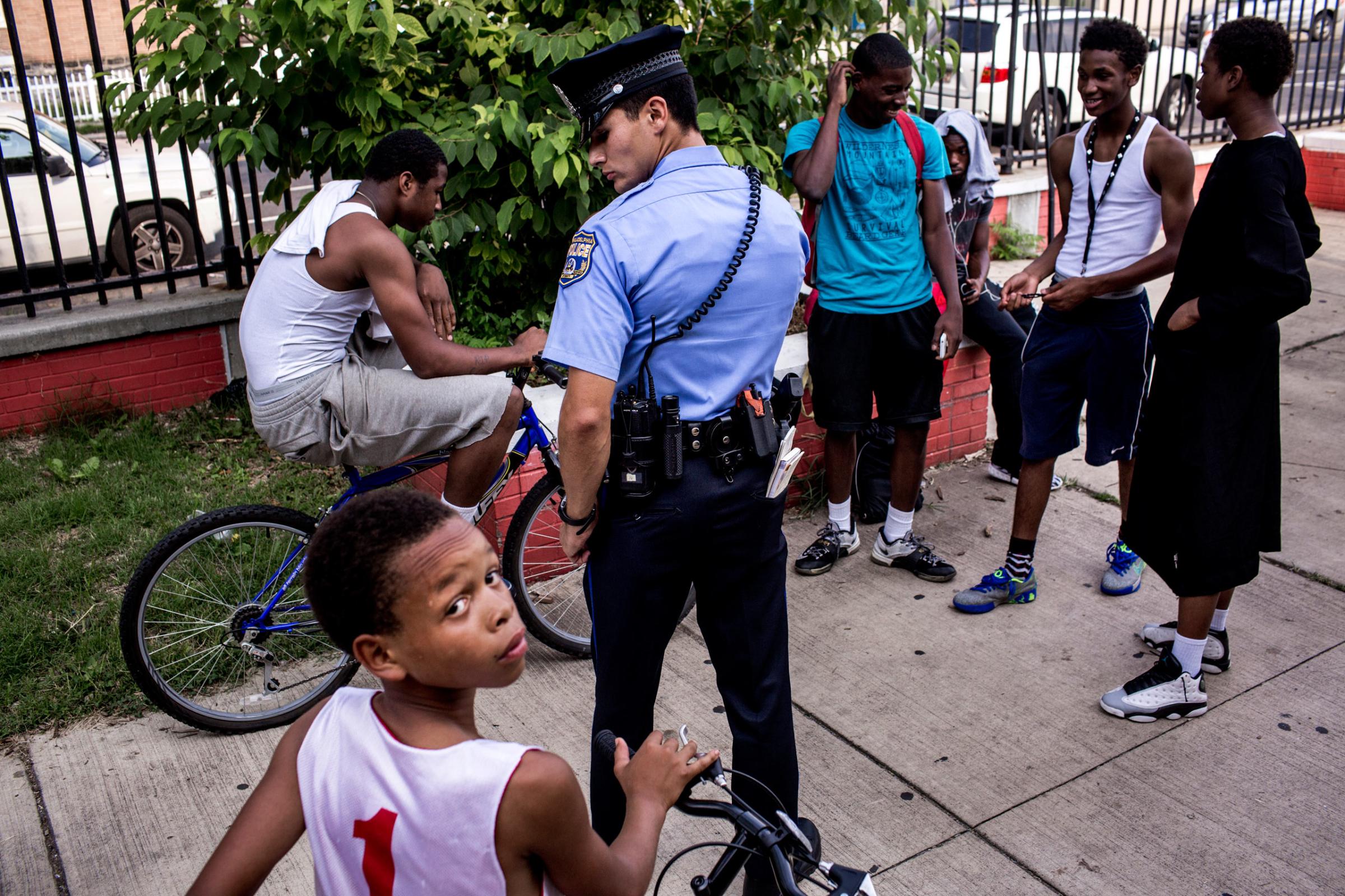 July 28th, 2015. Philadelphia, PA.  First year officer Jonathan Dedos (a "foot beat") questions a group of young men, after a shooting suspect was described as an african american wearing white and on a bike, a description which would imply the majority of young men in the neighborhood. This group, at a local park, was vouched for a by a man who works with local youth, and the police moved on. (Natalie Keyssar)