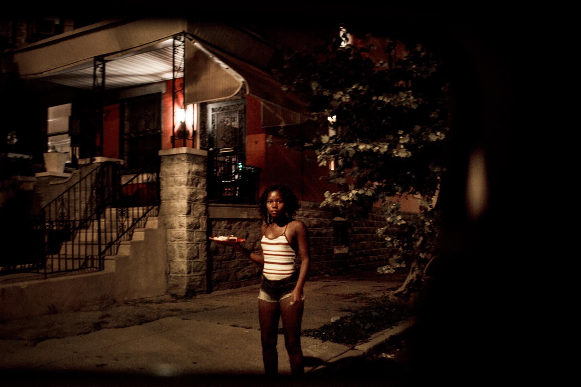 July 28th, 2015. Philadelphia, PA.  A young woman watches from a West Philadelphia corner as police drive by. (Natalie Keyssar)