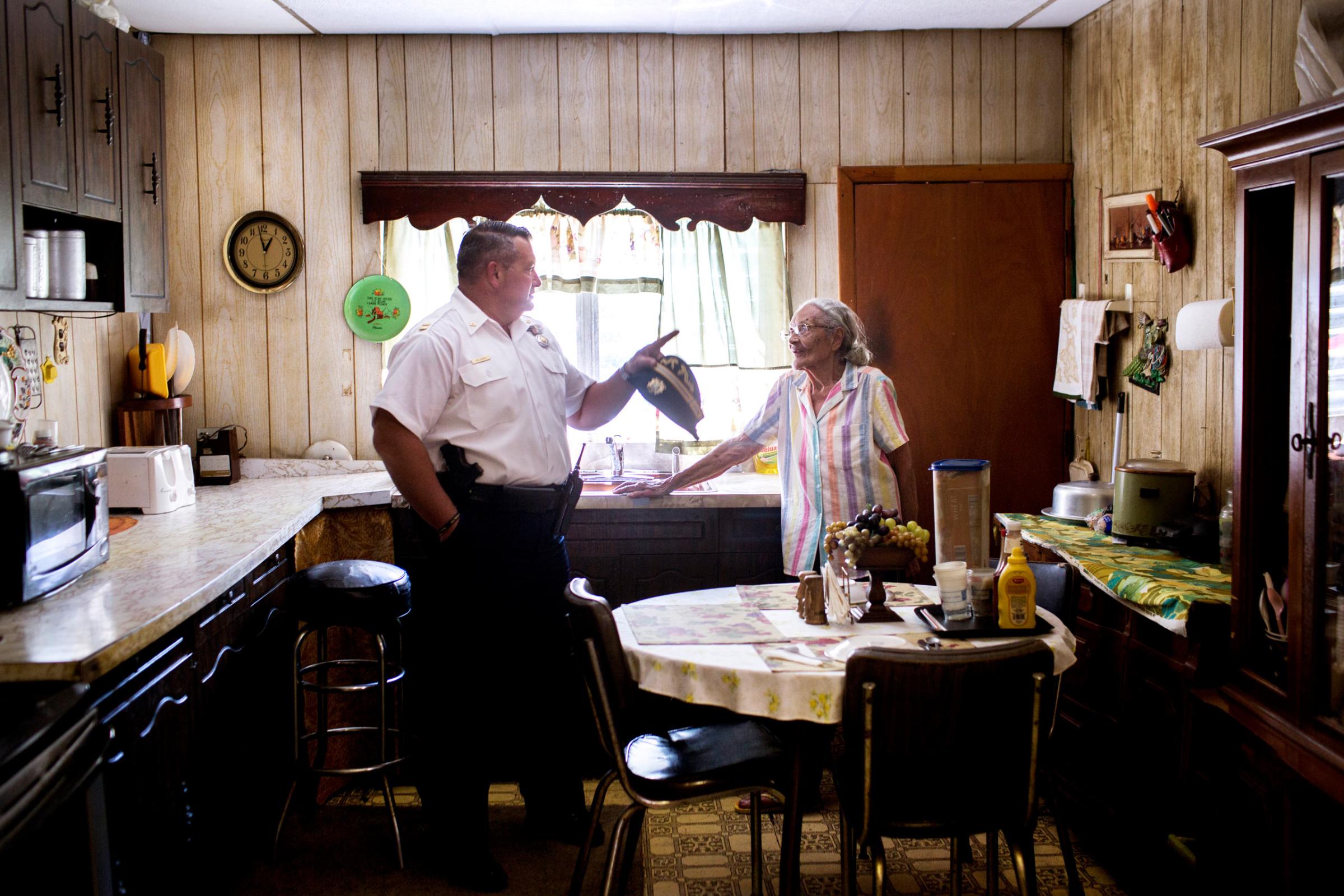 July 31th, 2015. Captain Joe Bologna chats with Louise Robinson in her kitchen after she called him in off the street to look at a problem with overgrowth in her back yard. Robinson has lived in her home down the street from the 19th District station since the 50's, and says that hers was one of the first black families to move to the neighborhood.