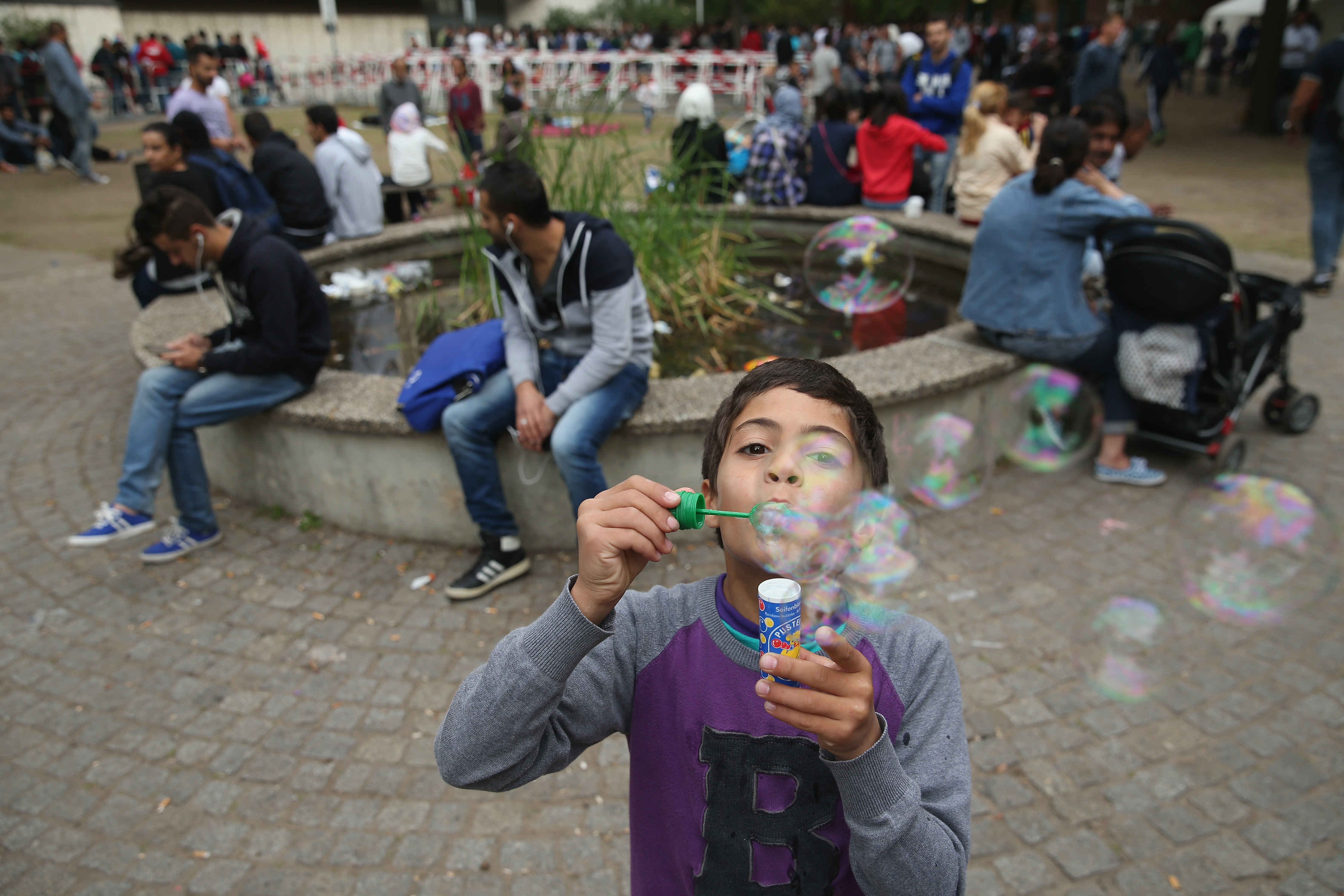 A young migrant boy from Syria blows soap bubbles as other migrants seeking asylum in Germany wait to register at the Central Registration Office for Asylum Seekers in Berlin on Aug. 27, 2015. (Sean Gallup—Getty Images)