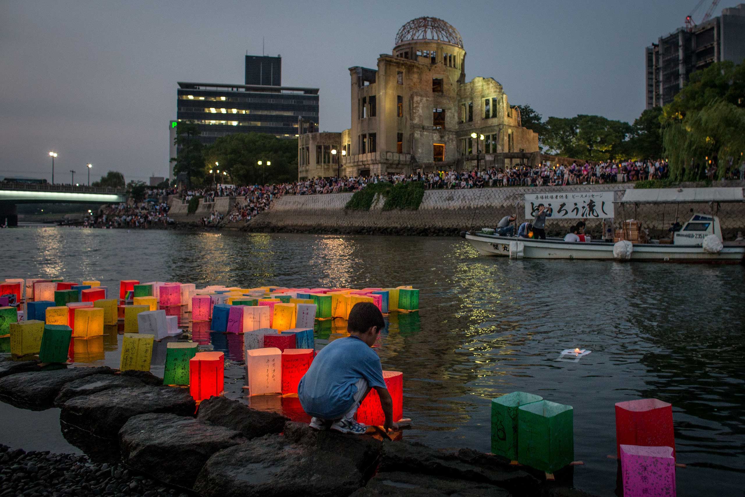 A boy floats a candle lit paper lantern on the river in front of the Atomic Bomb Dome  during 70th anniversary activities, commemorating the atomic bombing of Hiroshima at the Hiroshima Peace Memorial Park, on Aug.6, 2015