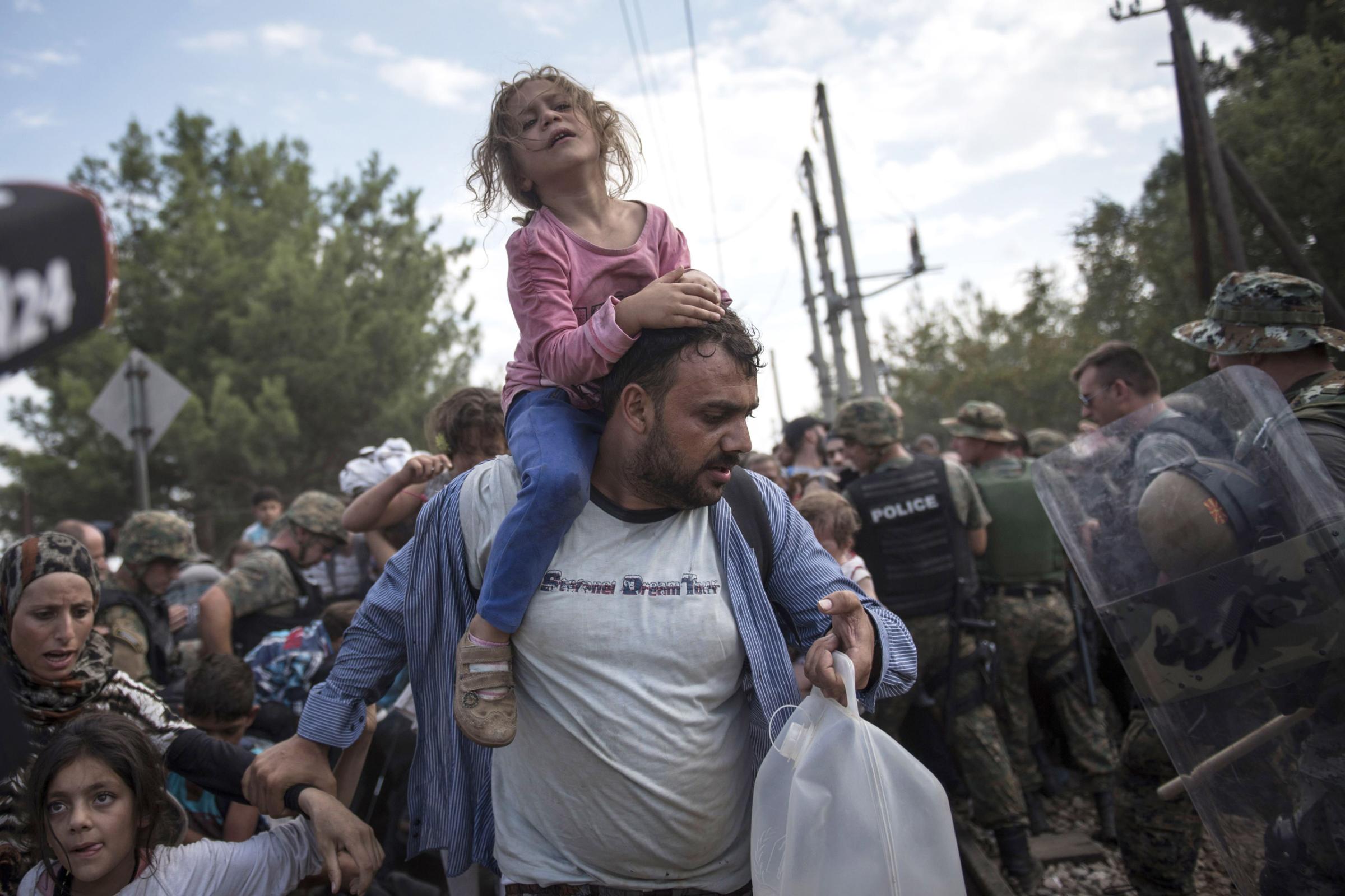 Mandatory Credit: Photo by NurPhoto/REX Shutterstock (2805163n) A migrant child and her father pass through the cordon of policeman and enter Macedonia, after they and other migrants were waiting on the Macedonian-Greek border where they are being held, since Macedonia declared emergency at its borders and closed its south border for them Macedonia blocks its border with Greece, Gevgelija, Macedonia - 21 Aug 2015 Thousands of them are being held in the zone between Greece and Macedonia.
