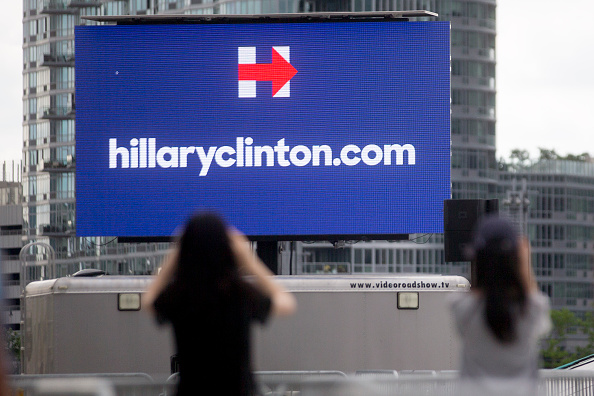 Visitors take a photograph of a Hillaryclinton.com billboard before the first 2016 Democratic candidate Hillary Clinton campaign rally at Four Freedoms Park on Roosevelt Island in New York, U.S., on Saturday, June 13, 2015.