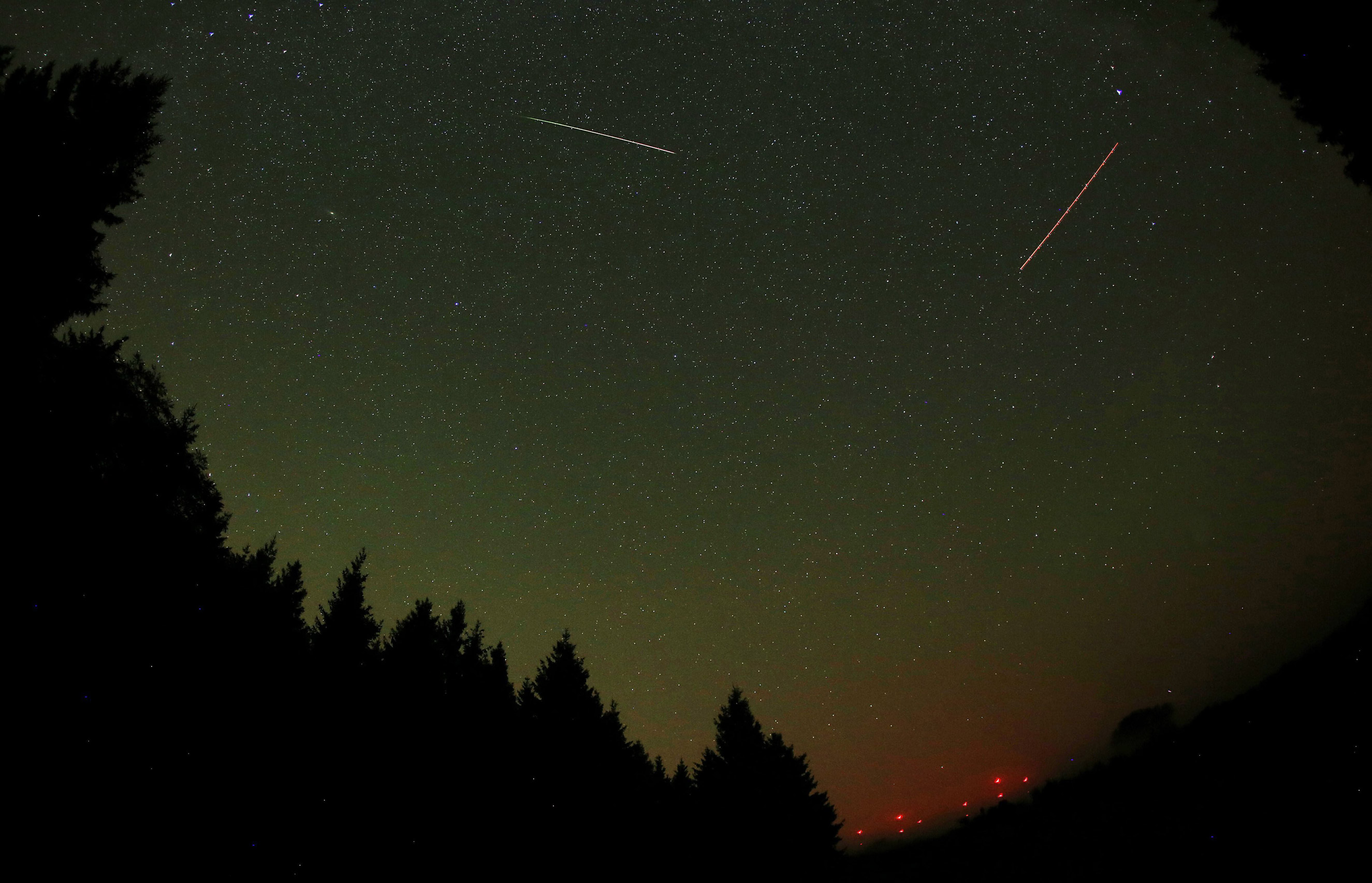 A meteor from the Perseid meteor shower (left) and the lights from a plane (right) streak across the sky near Gemuend, Germany on Aug. 13, 2015.