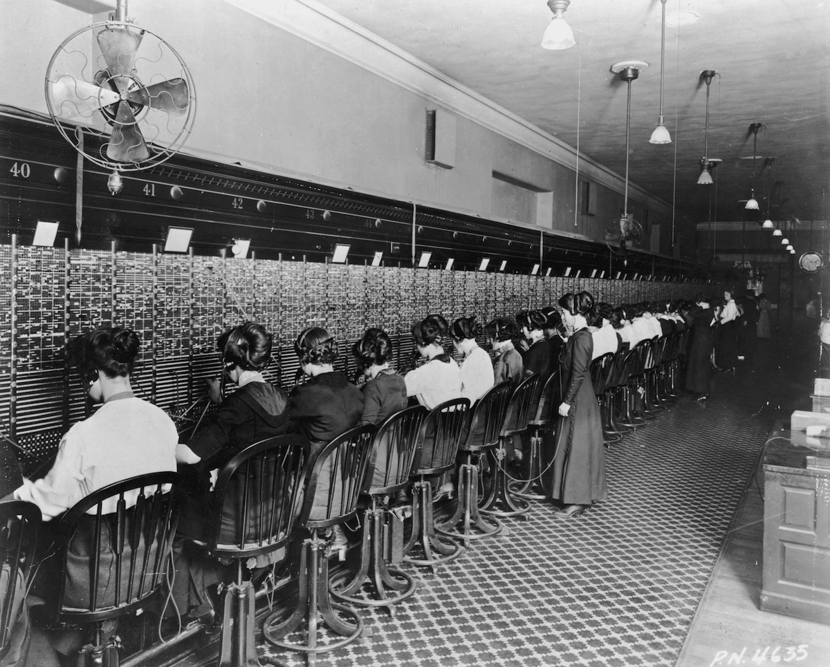 Telephone operators sitting in front of a long switchboard at the Cortlandt Exchange in New York City around the turn of the century