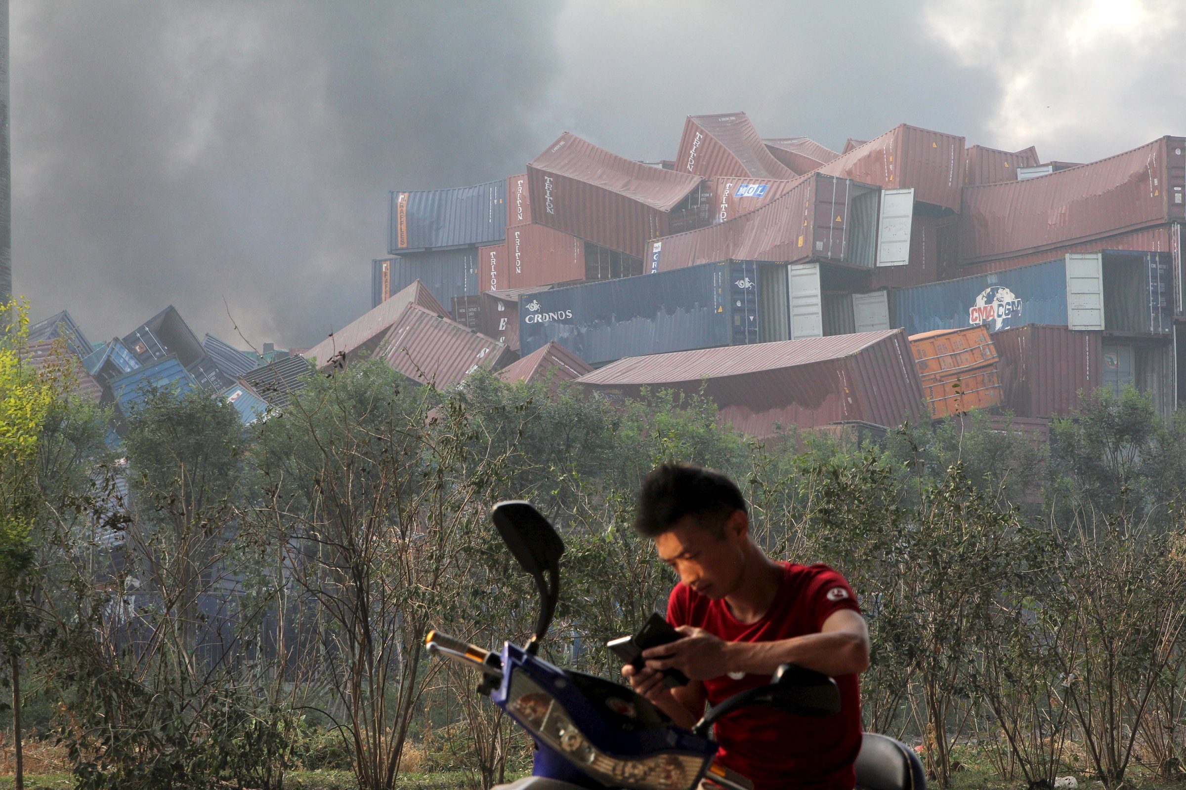 A man checks his mobile phone near overturned shipping containers after explosions in Tianjin