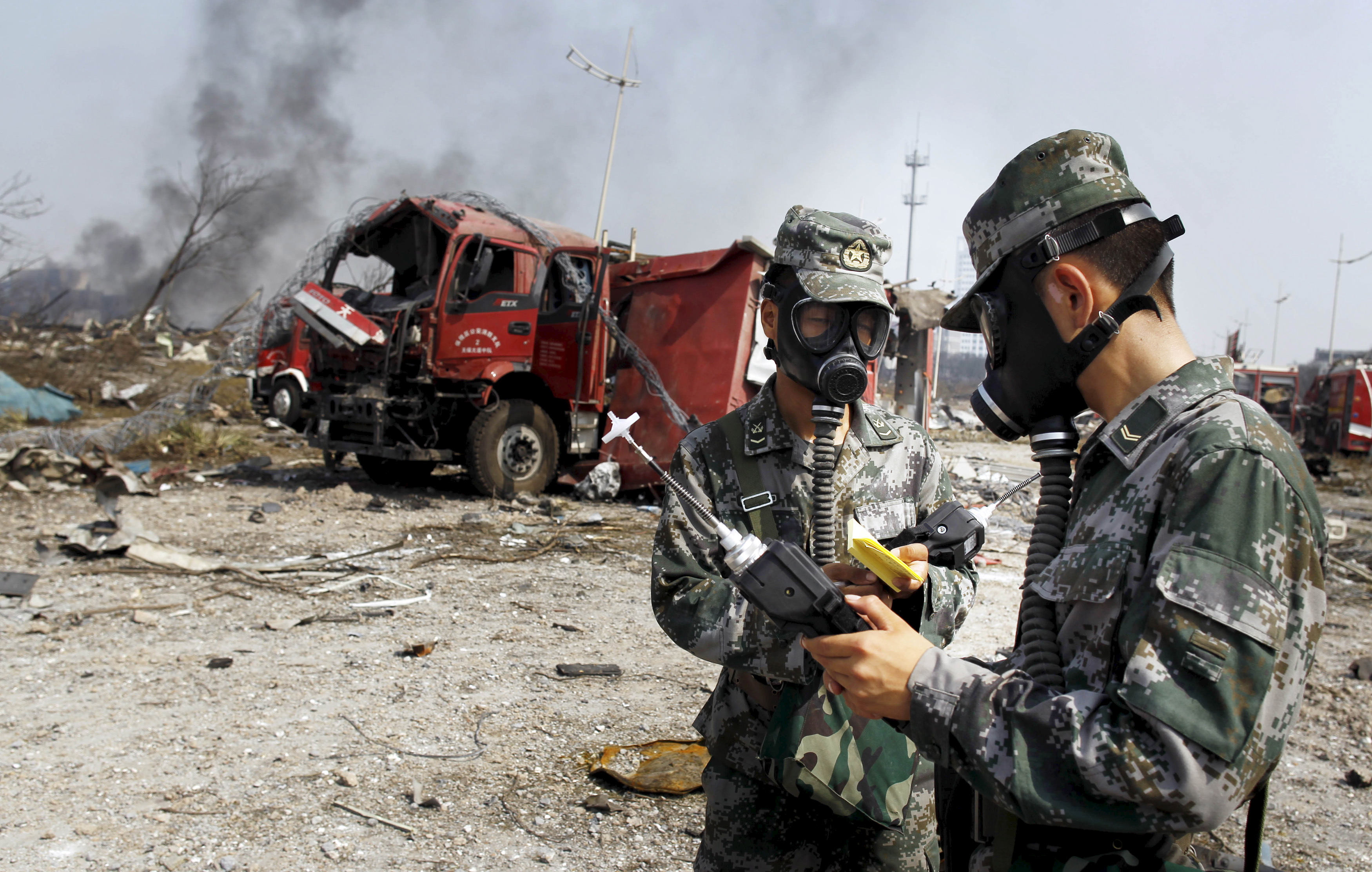 Soldiers of the People's Liberation Army anti-chemical warfare corps work next to a damaged firefighting vehicle at the site of Wednesday night's explosions at Binhai new district