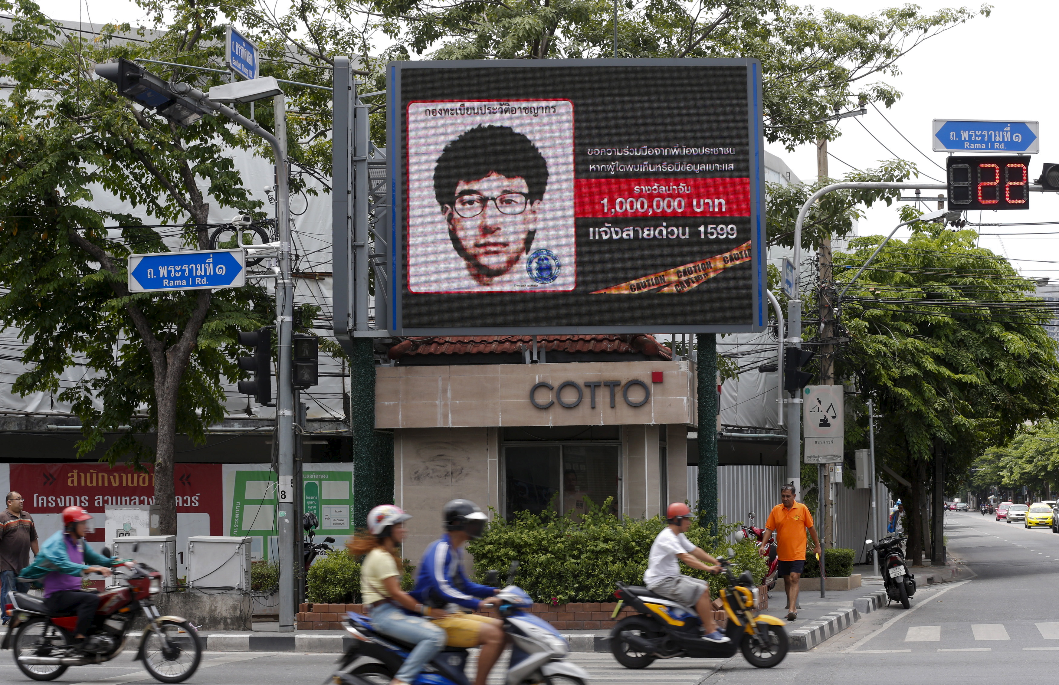People ride their motorcycles past a digital billboard showing a sketch of the main suspect in Monday's attack on Erawan shrine, in Bangkok, Thailand