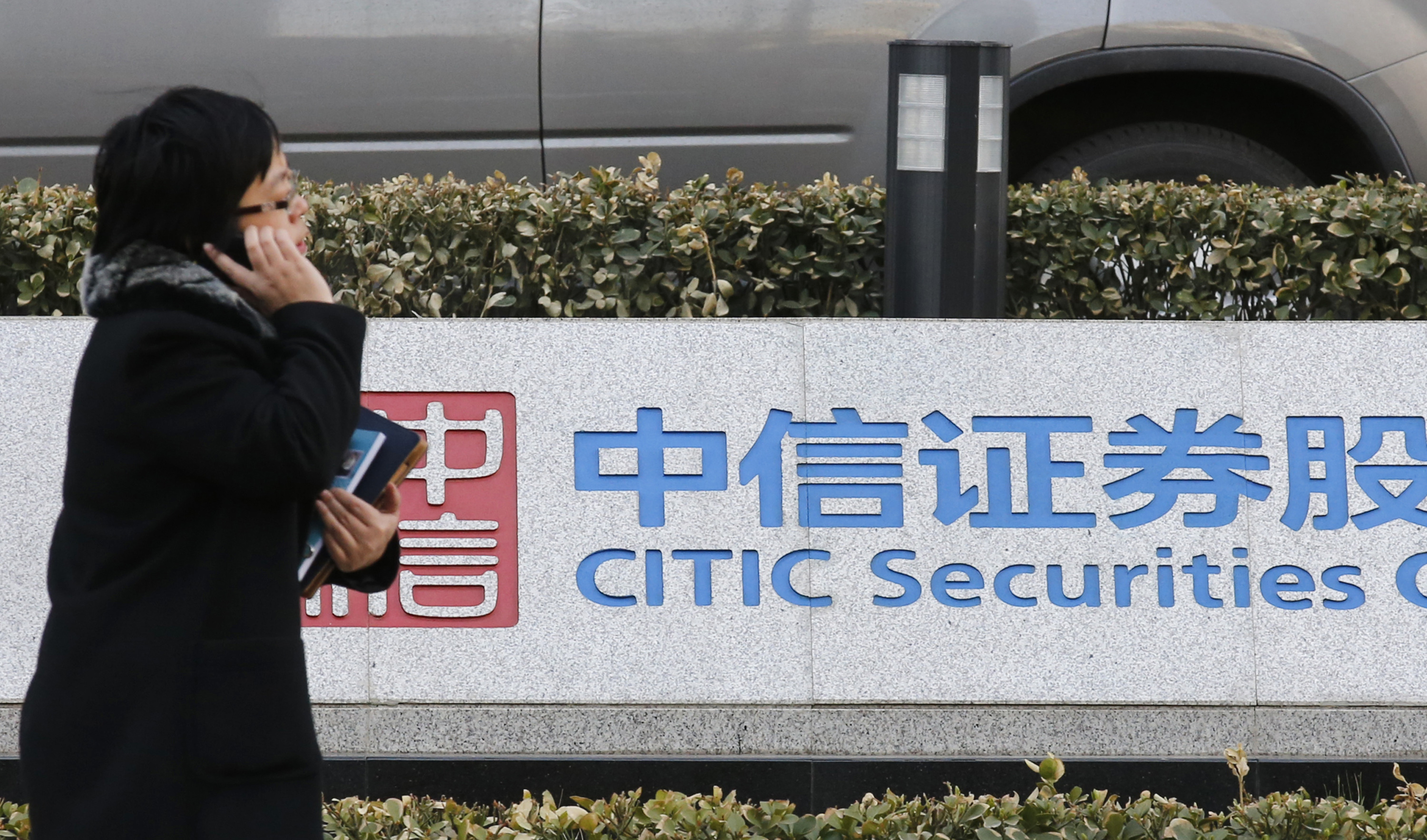 A woman walks past a signboard of CITIC Securities at its head office in Beijing