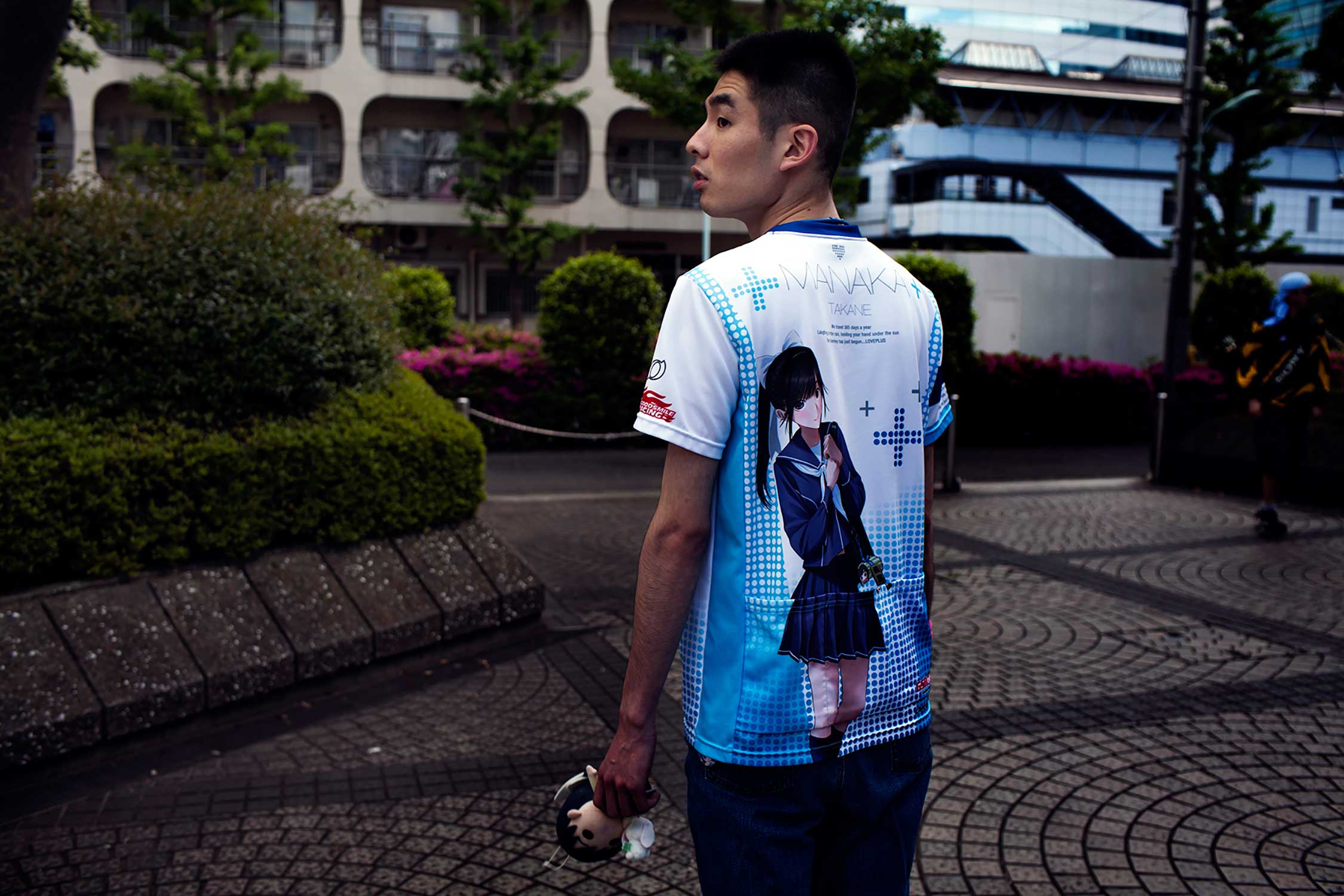 25-year old Love Plus player Naoki who works as a train station guard, wears a t-shirt with a print of his virtual girlfriend Manaka and holds a doll made to her resemblance. (Loulou d’Aki)