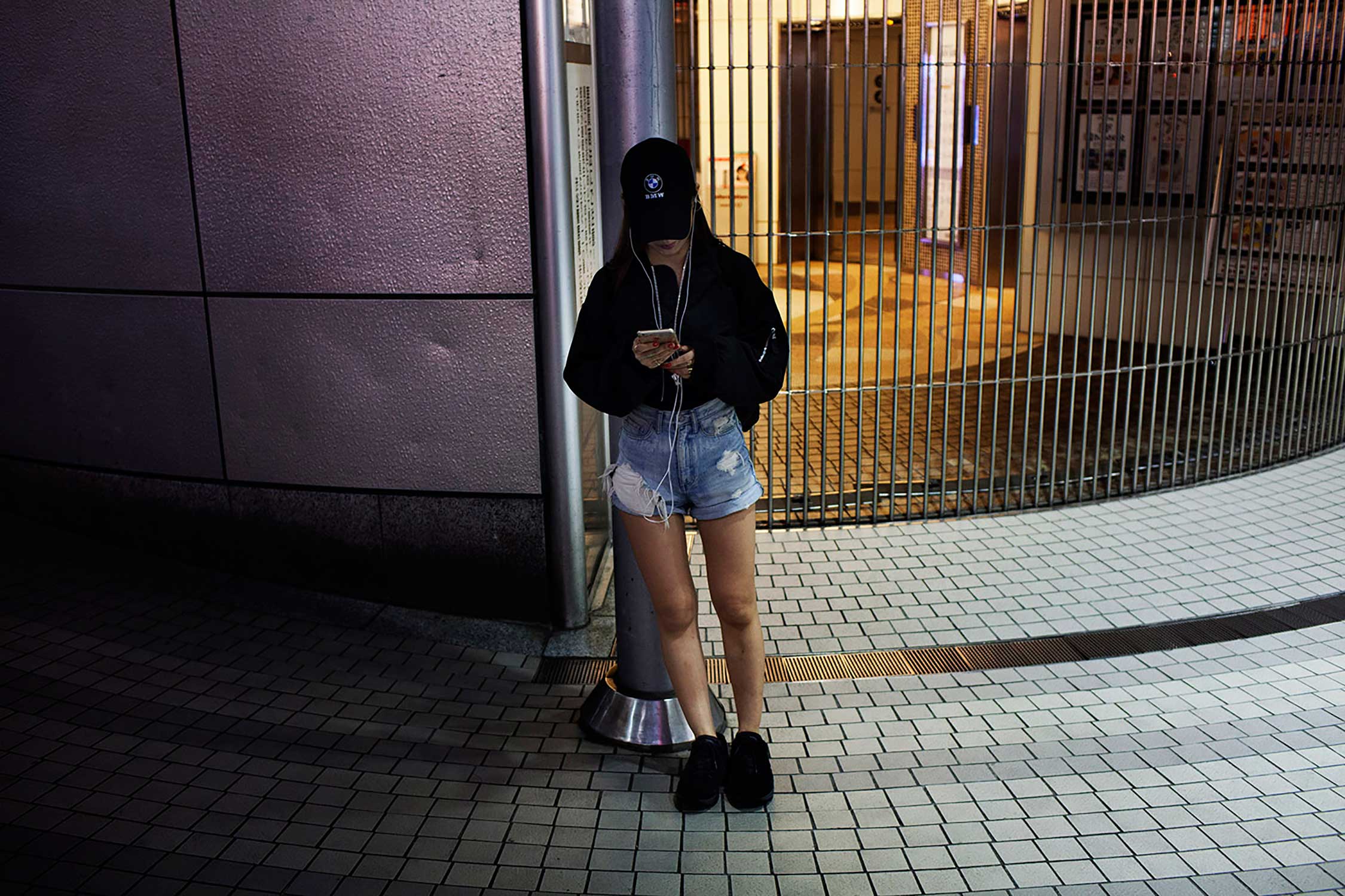A girl spends time with her iphone as she waits by Shibuya on a Friday night.