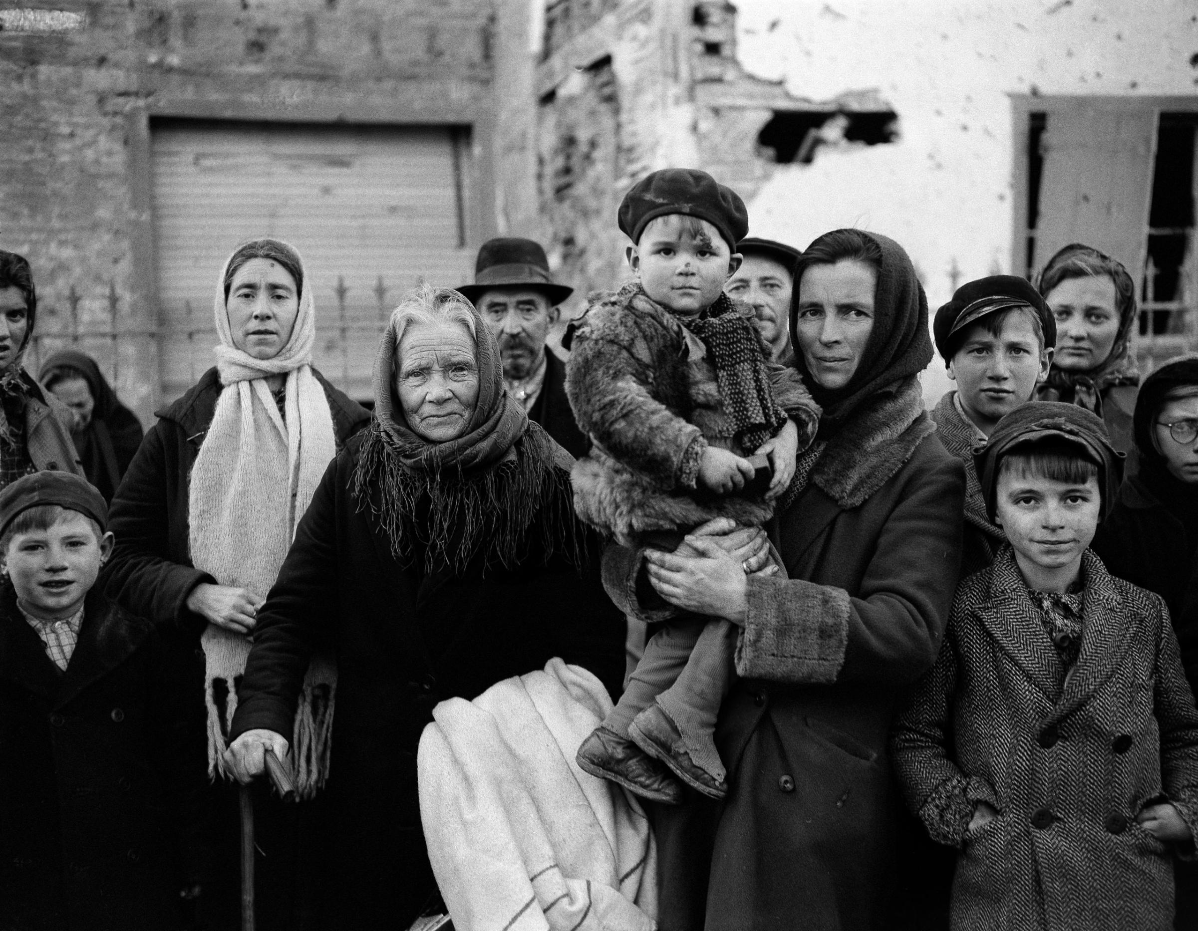 Grim-faced refugees stand in a group on a street in La Gleize, Belgium on Jan. 2, 1945. They are waiting to be transported from the war-torn town after its recapture by American forces during the German thrust into the Belgium-Luxembourg salient.