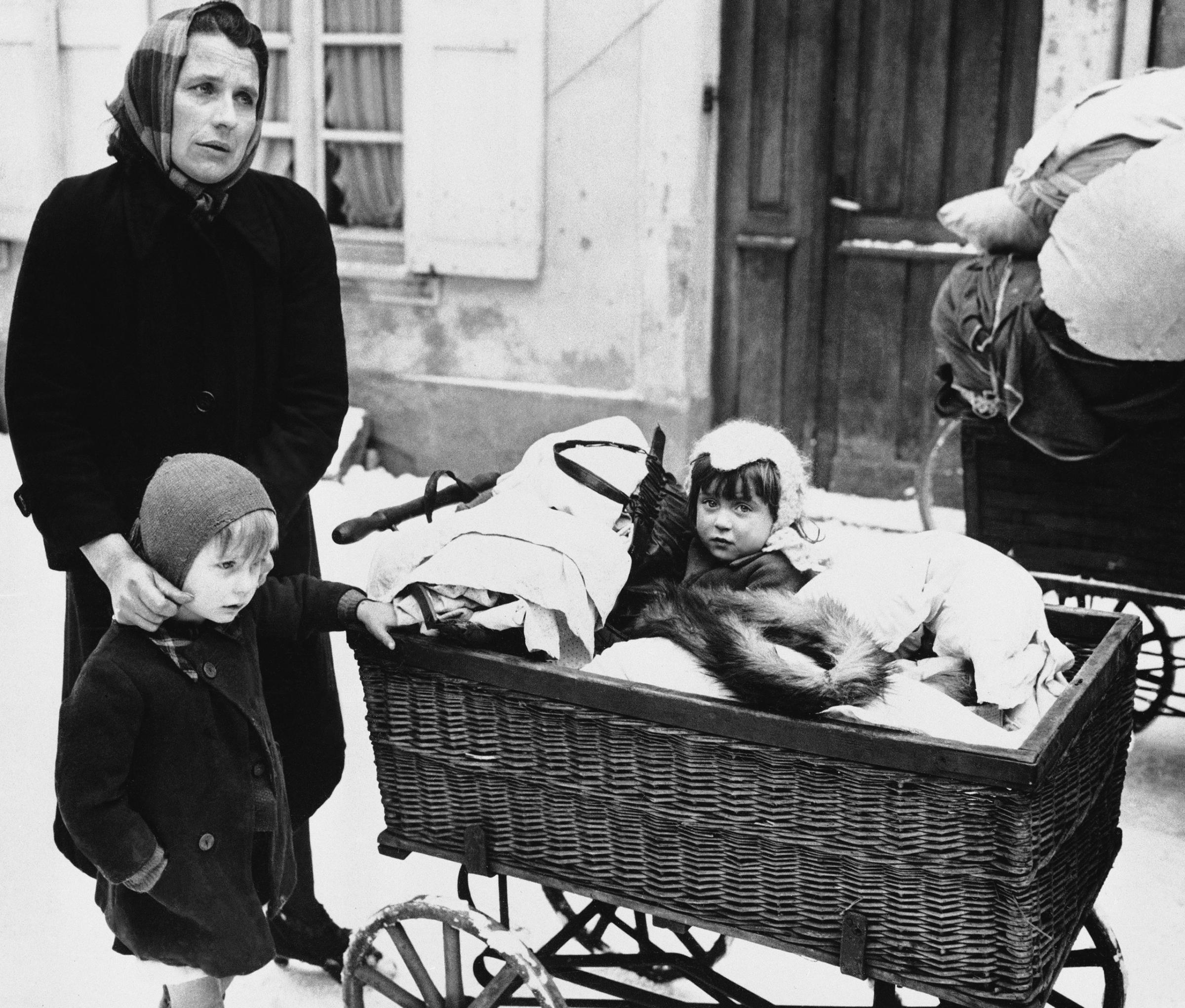 Frenchwoman with two children and belongings loaded on a baby carriage seen in Haguenau, France on Feb. 20, 1945, before they started on their long trek to a safe rear area. They are some of the refugees leaving the town because of the planned withdrawal of the 7th U.S. Army. Many civilians prefer to leave their homes and seek safety in a rear area, rather than suffer another German occupation or risk being conscripted into the German Vollksturn.