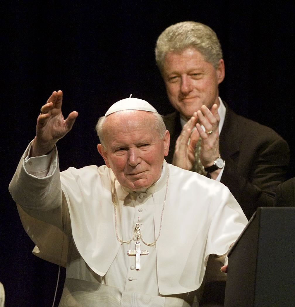Pope John Paul II waves as US President Bill Clinton applauds during an arrival ceremony on January 26, 1999 at Lambert International Airport in St. Louis, Missouri.