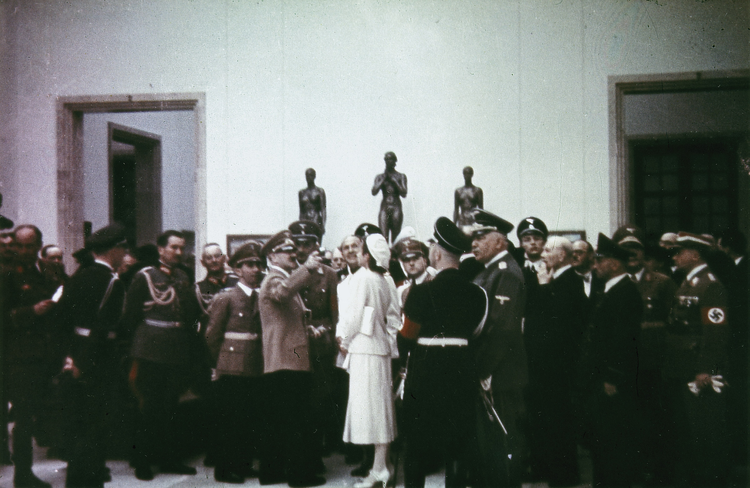 Photograph by Heinrich Hoffmann of Gerdy Troost speaking with Hitler and surrounded by a crowd of Nazi bigwigs at the House of German Art in Munich on the Day of German Art, July 16, 1939. Those pictured (from left to right): Eugen von Schobert, Joseph Goebbels, Adolf Hitler, Dino Alfieri, Gerdy Troost, Heinrich Himmler (back turned), Konstantin von Neurath.