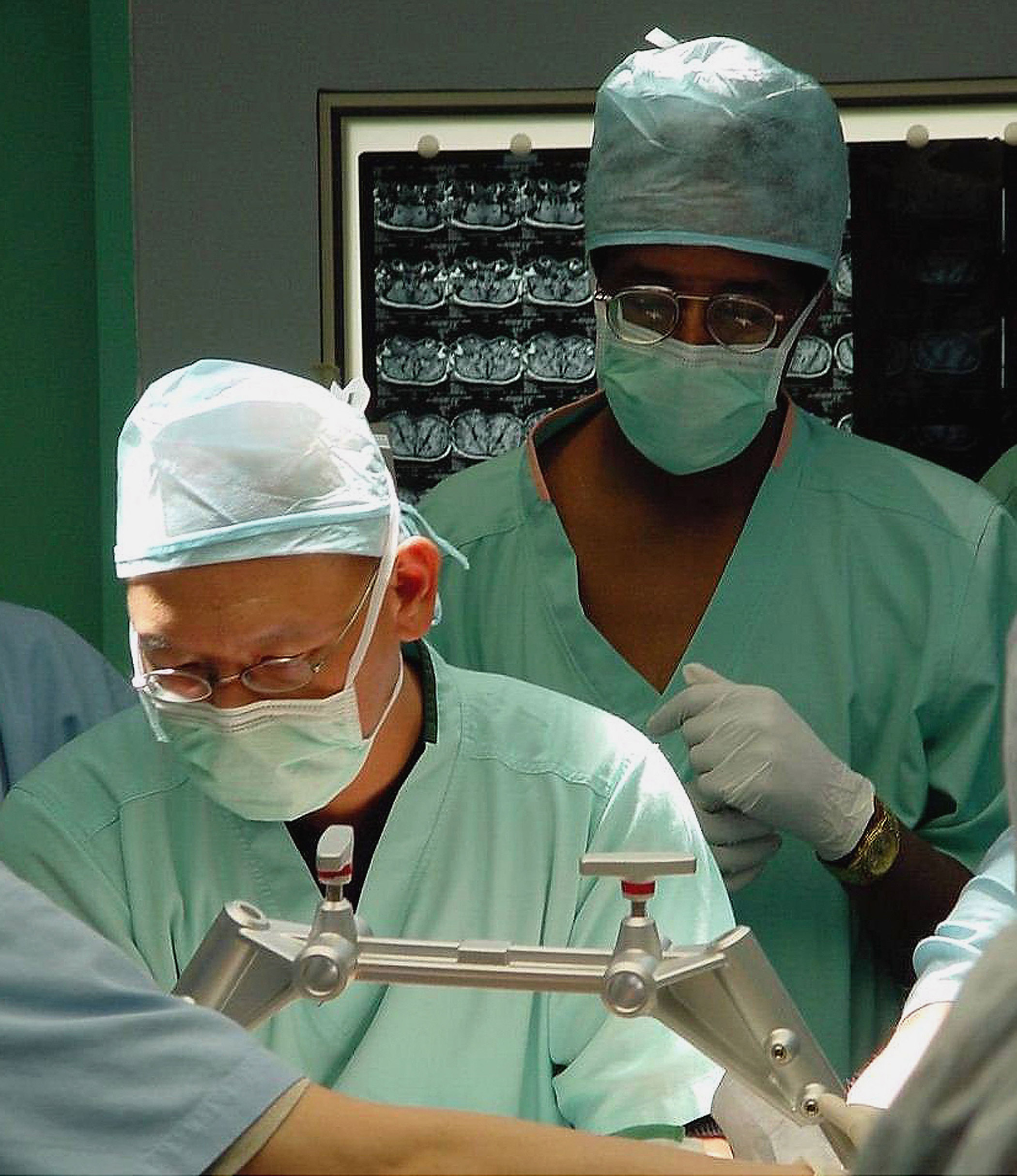 Dr. Keith Goh (left) adjusts the frame on conjoined twins Ladan and Laleh Bijani as Dr. Ben Carson observes the start of neurosurgery proceedings at the Raffles Hospital on July 6, 2003 in Singapore.