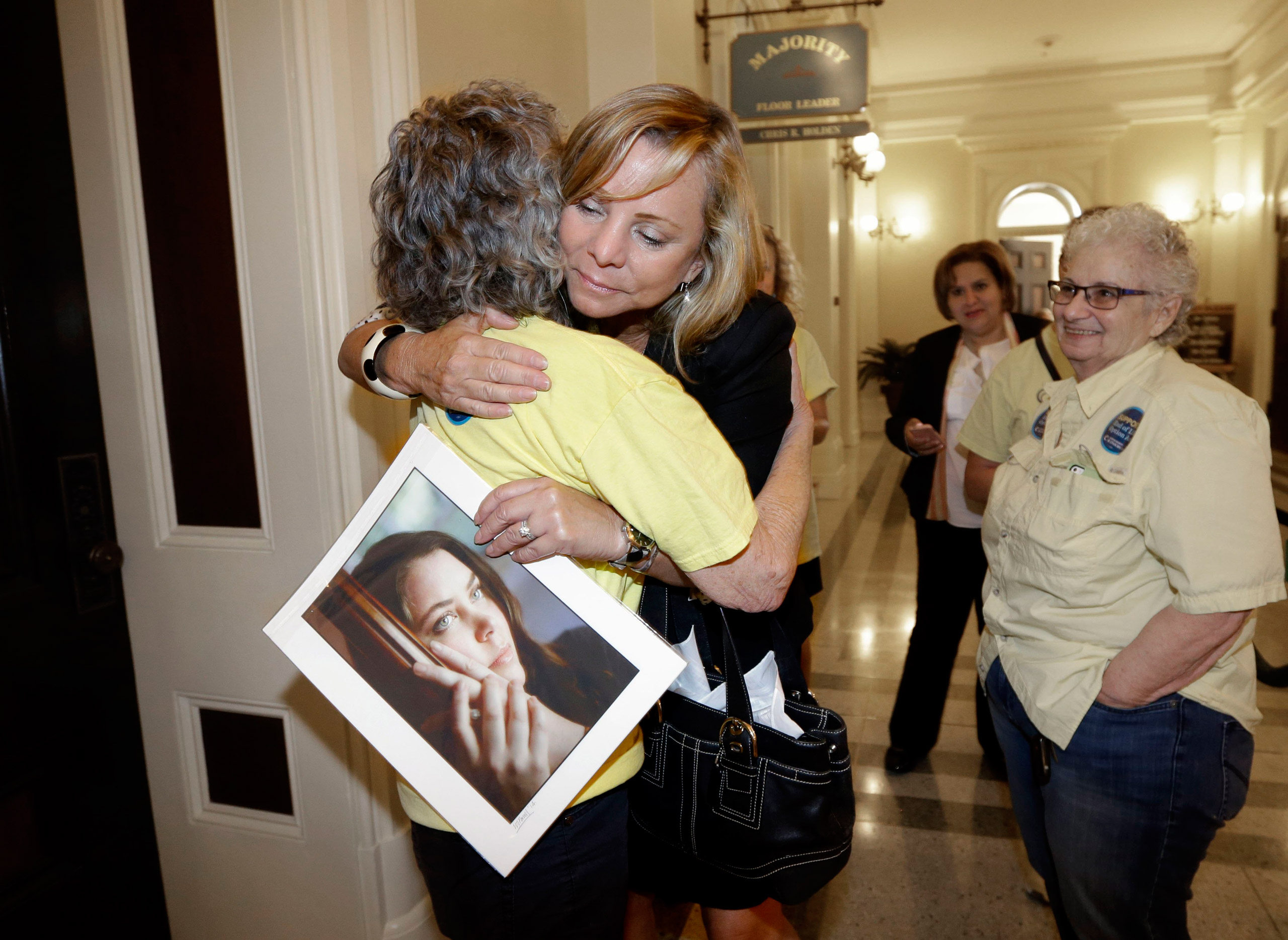 Debbie Ziegler holds a photo of her daughter, Brittany Maynard, as she receives congratulations from Ellen Pontac, after a right-to die measure was approved by the state Assembly, Wednesday, Sept. 9, 2015, in Sacramento, Calif. The bill, approved on a 42-33 vote, that would allow terminally ill patients to legally end their lives, now goes to the Senate.  Brittany Maynard was the California woman with brain cancer who moved to Oregon to legally end her life last fall. (AP Photo/Rich Pedroncelli)
