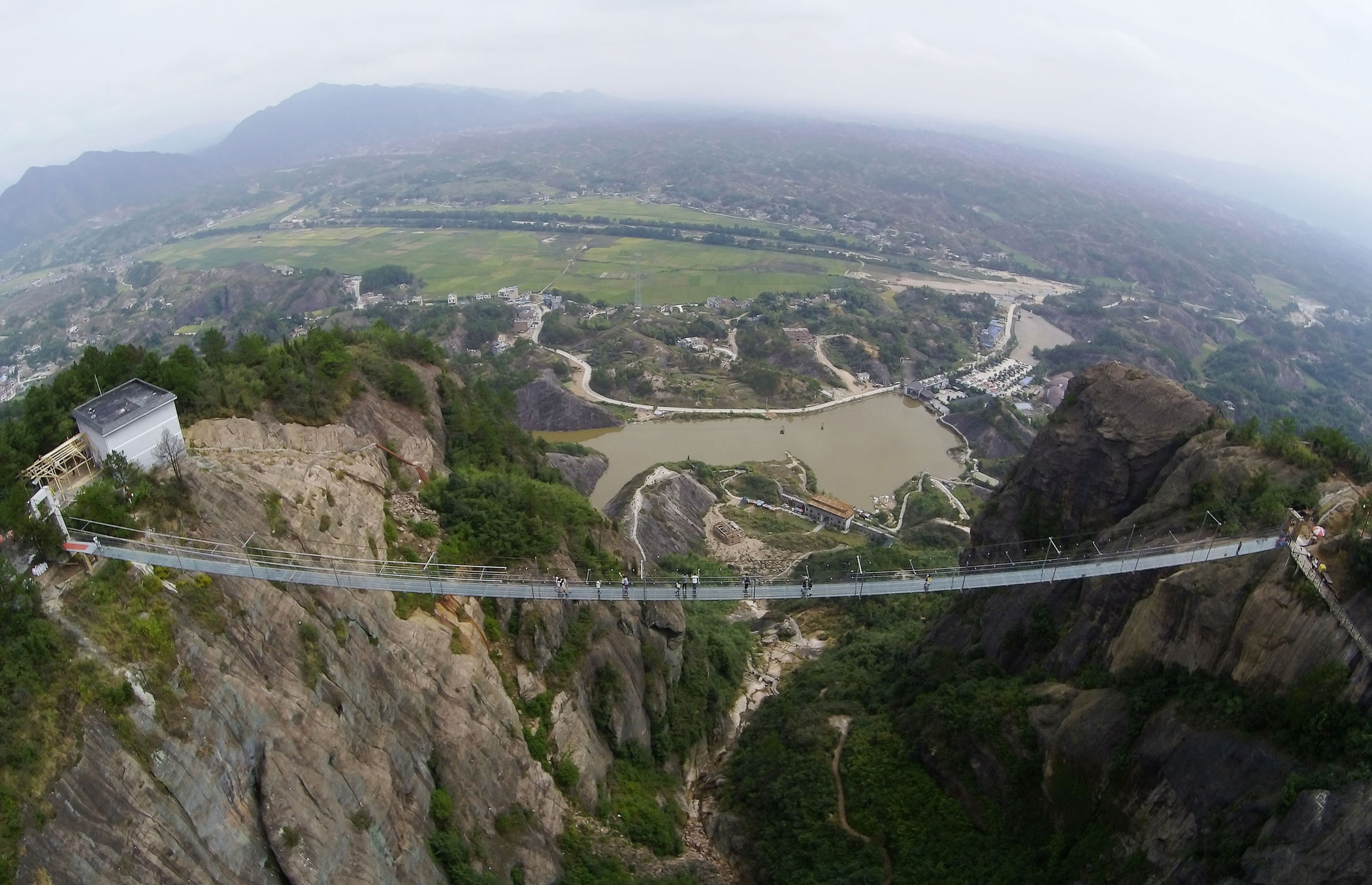 PINGJIANG, CHINA - SEPTEMBER 24:  (CHINA OUT) Tourists walk on a suspension bridge made of glass at the Shiniuzhai National Geological Park on September 24, 2015 in Pingjiang County, China. The 300-meter-long glass suspension bridge, with a maximum height of 180 meters, opened to the public on Thursday.  (Photo by ChinaFotoPress/ChinaFotoPress via Getty Images)