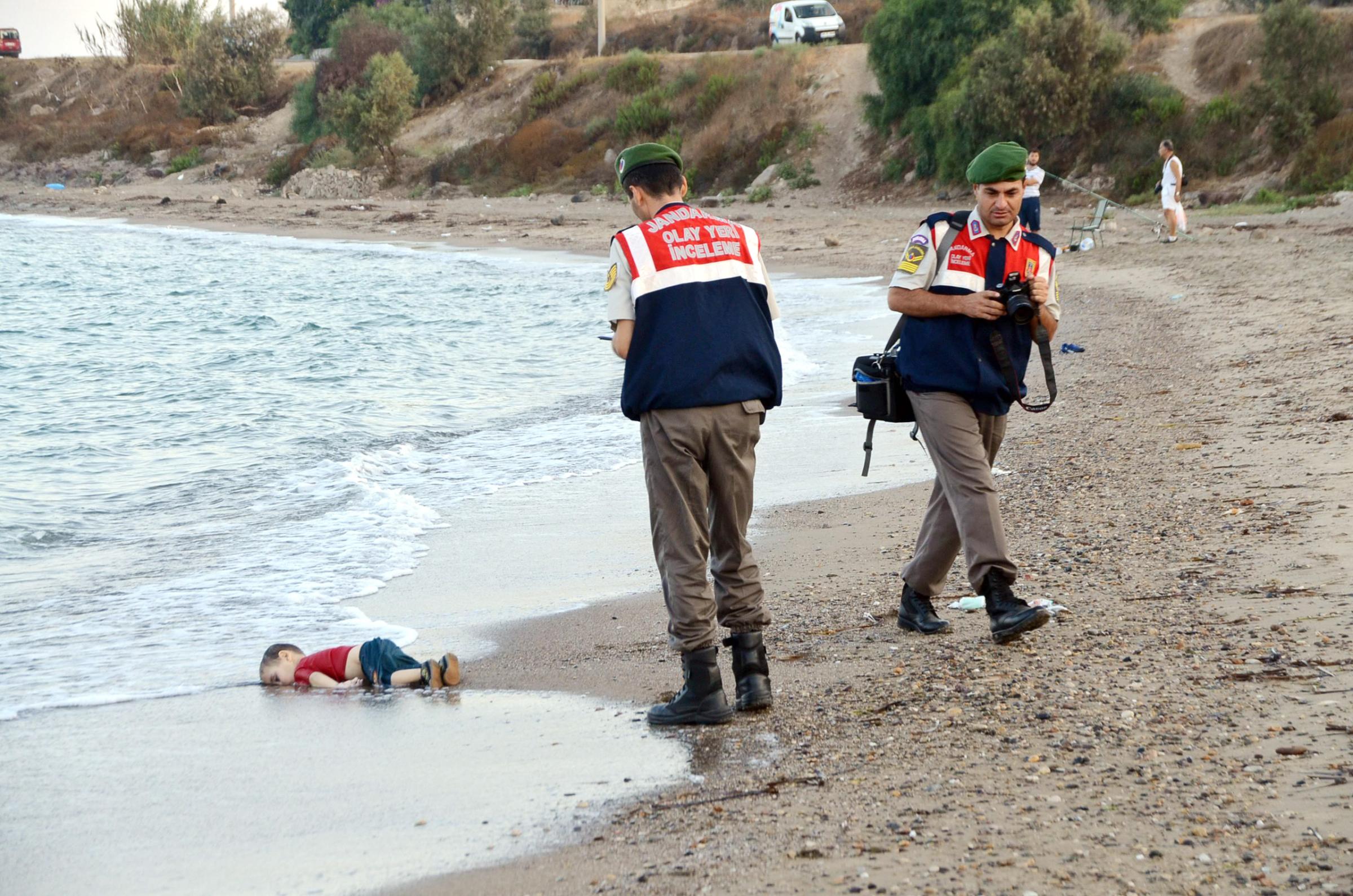 Members of the Turkish gendarmerie stand near by the washed-up body of a refugee child who drowned during a failed attempt to sail to the Greek island of Kos, at the shore in the coastal town of Bodrum, Turkey, on Sept. 2, 2015. At least 11 Syrian migrants died in boat sank after leaving Turkey for the Greek island of Kos.