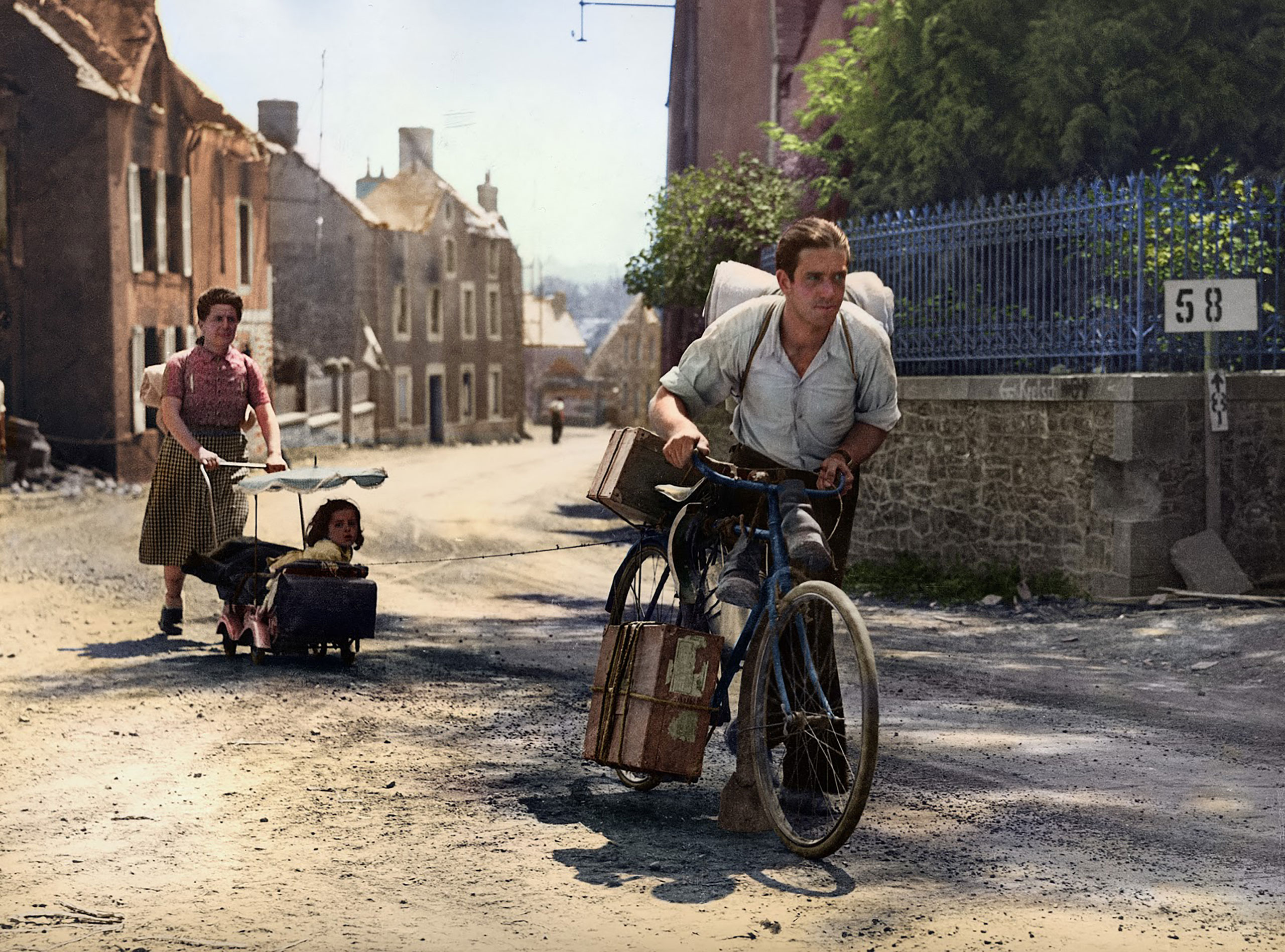 A man pulls a refugee's pram, attached by a cord to his bike, up a hill in Roncey, France on August 7, 1944.