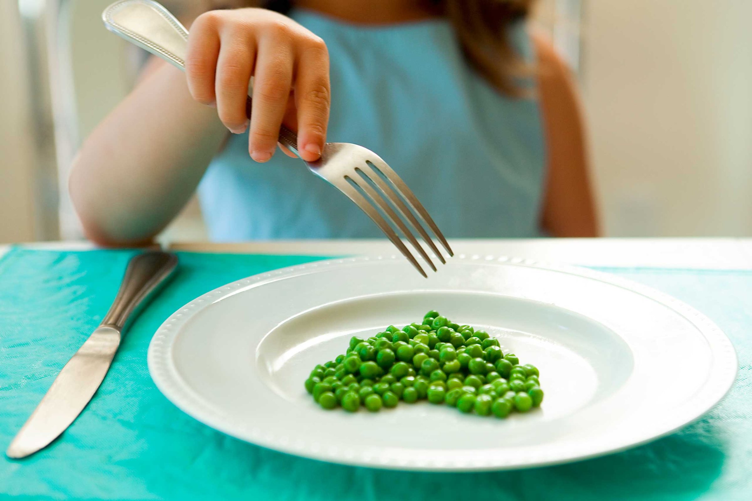 Girl eating green peas with a fork