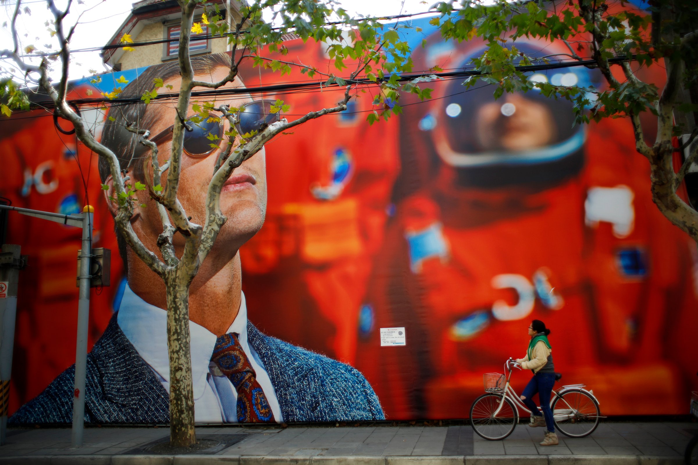 A woman looks at a giant billboard for a clothing shop, as she rides her bike along a street in downtown Shanghai