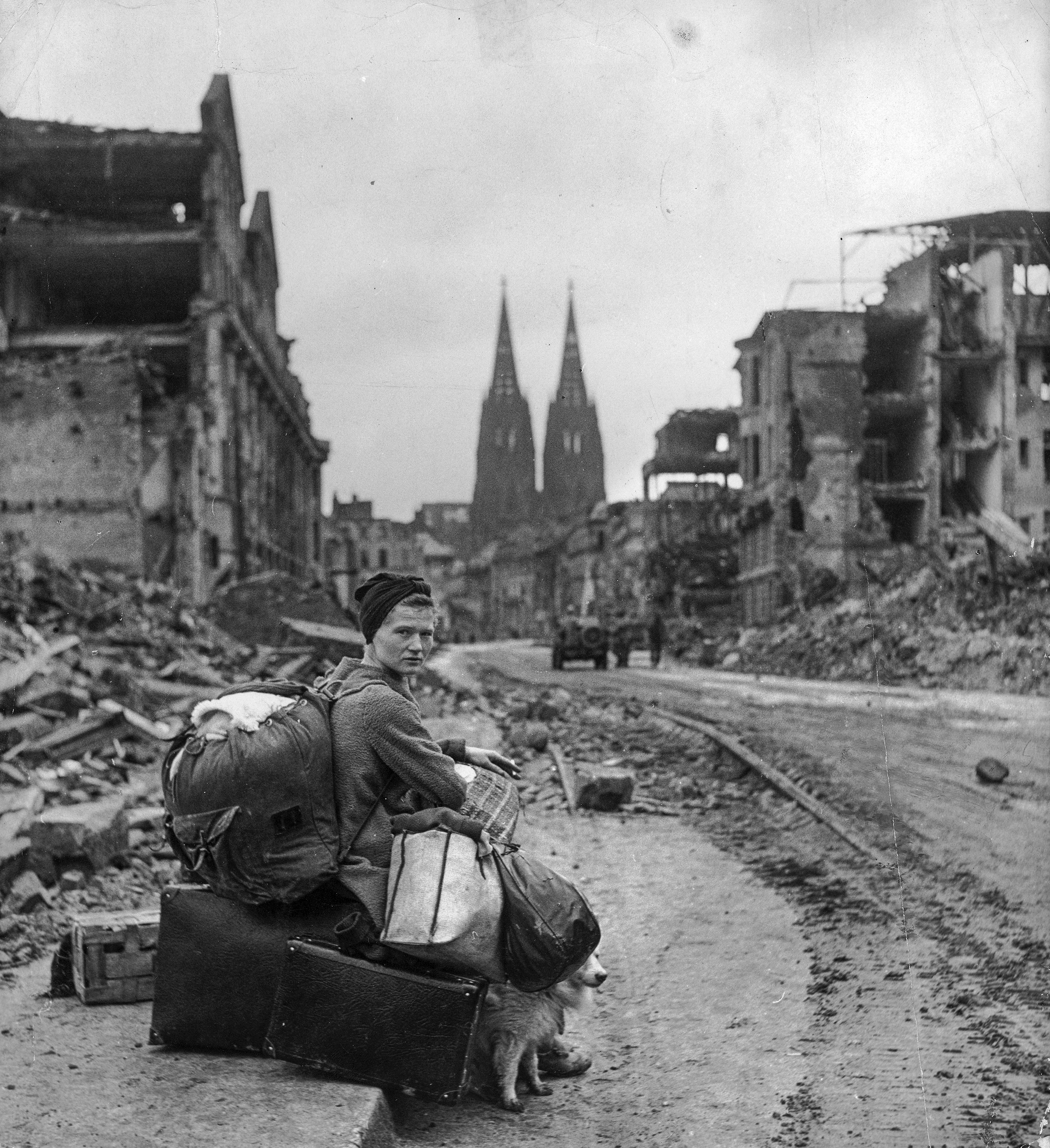 A homeless refugee German woman sits with all of her possessions on the side of a muddy street in Cologne amid ruins caused by massive Allied air raids, March 1945.