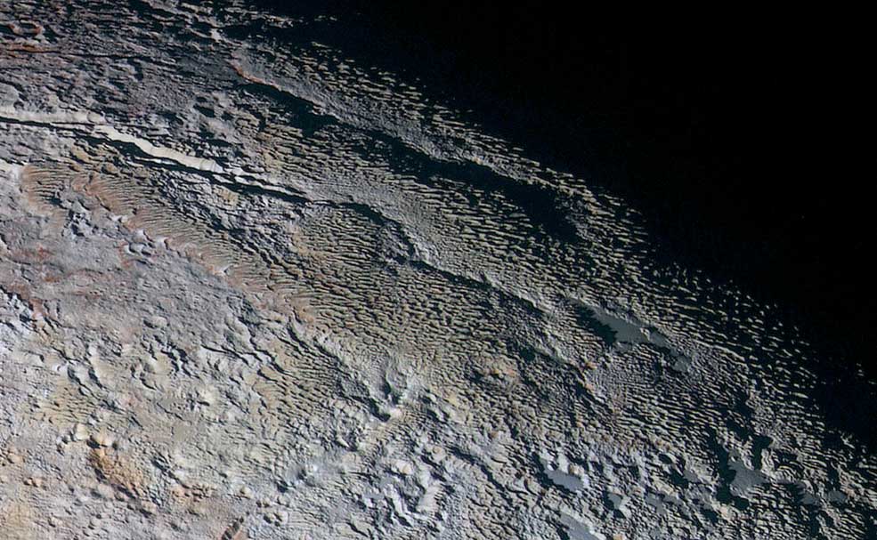 In this extended color image of Pluto taken by NASA’s New Horizons spacecraft, rounded and bizarrely textured mountains, informally named the Tartarus Dorsa, rise up along Pluto’s day-night terminator and show intricate but puzzling patterns of blue-gray ridges and reddish material in between. This view, roughly 330 miles (530 kilometers) across, combines blue, red and infrared images taken by the Ralph/Multispectral Visual Imaging Camera (MVIC) on July 14, 2015, and resolves details and colors on scales as small as 0.8 miles (1.3 kilometers). (NASA/JHUAPL/SWRI)
