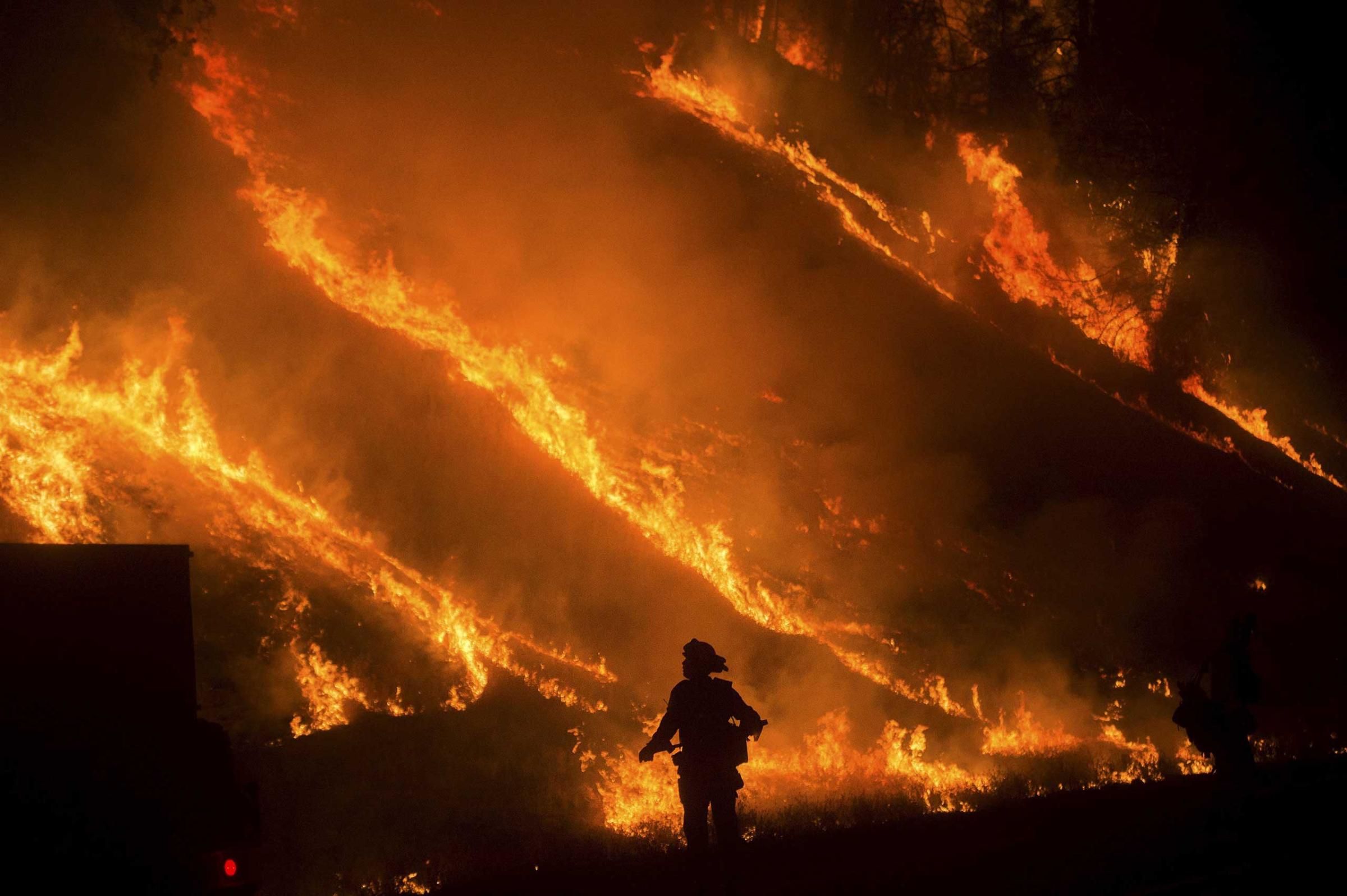 Flames from a backfire on Highway 29 rise above a firefighter battling the Valley Fire in Lower Lake