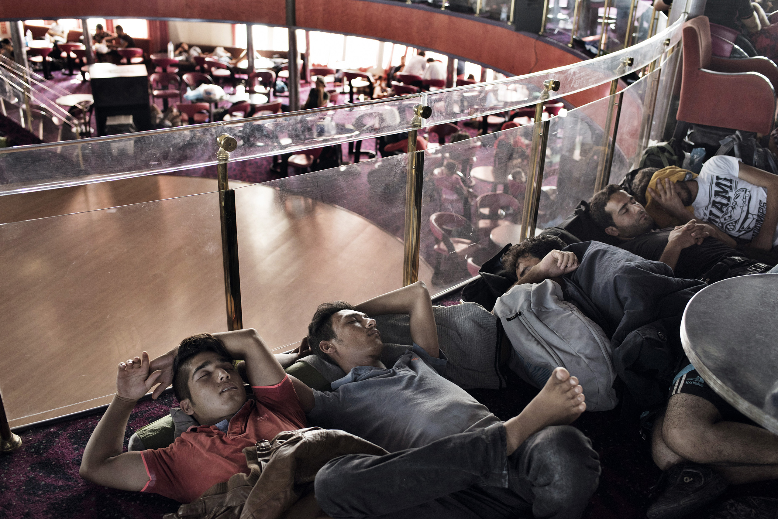 Migrants rest and recharge their phones aboard a cruise ship that the Greek government chartered to transport them to Athens from the Greek island of Lesbos. The regular ferry service traveling this route was unable to cope with the unprecedented influx of migrants going through Greece to Western Europe from various conflict zones across the Muslim world.