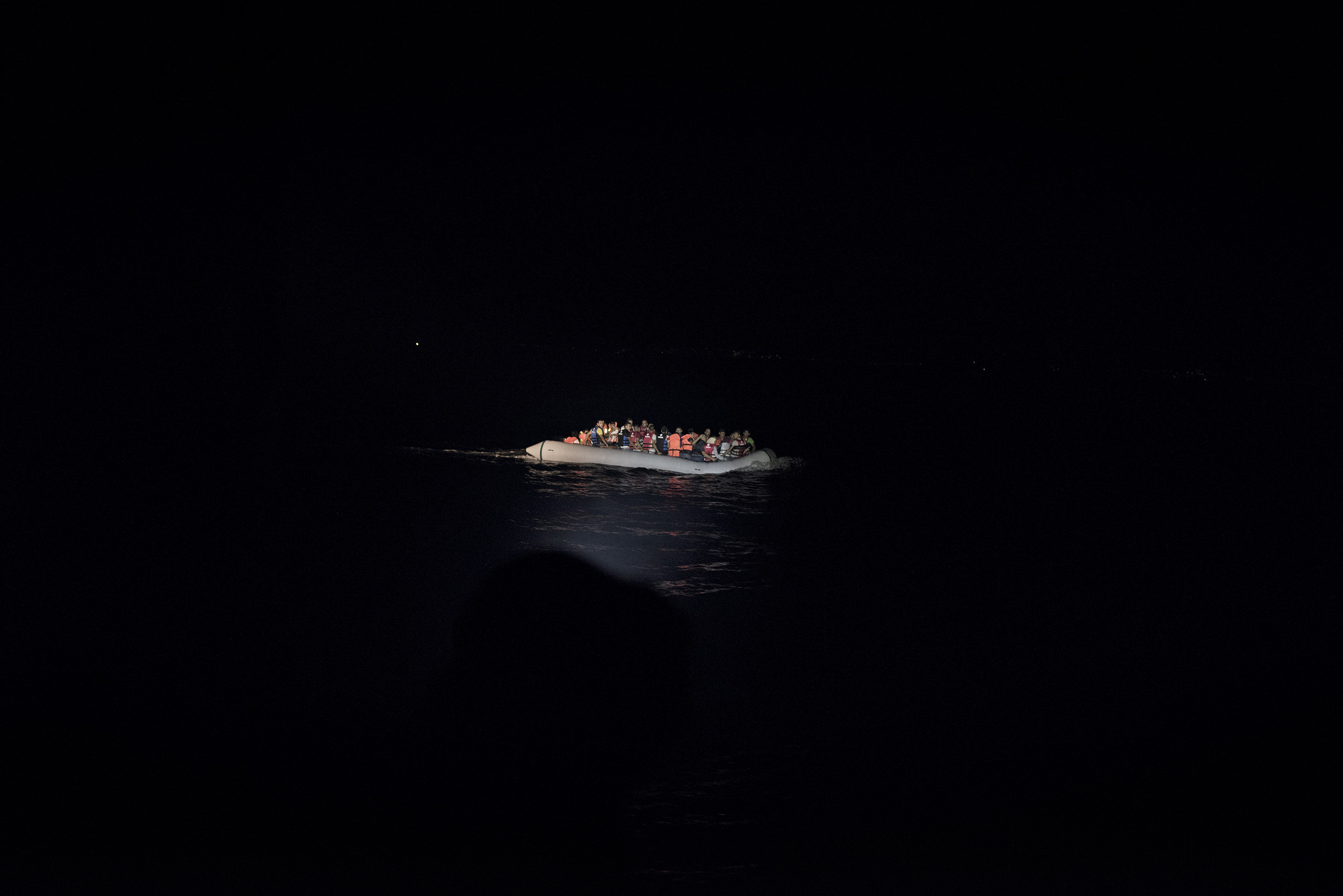 A boat full of migrants is illuminated by the flash lights of Greek coast guards who have come to rescue them from the waters near the Greek-Turkish border. Sept. 7, 2015.