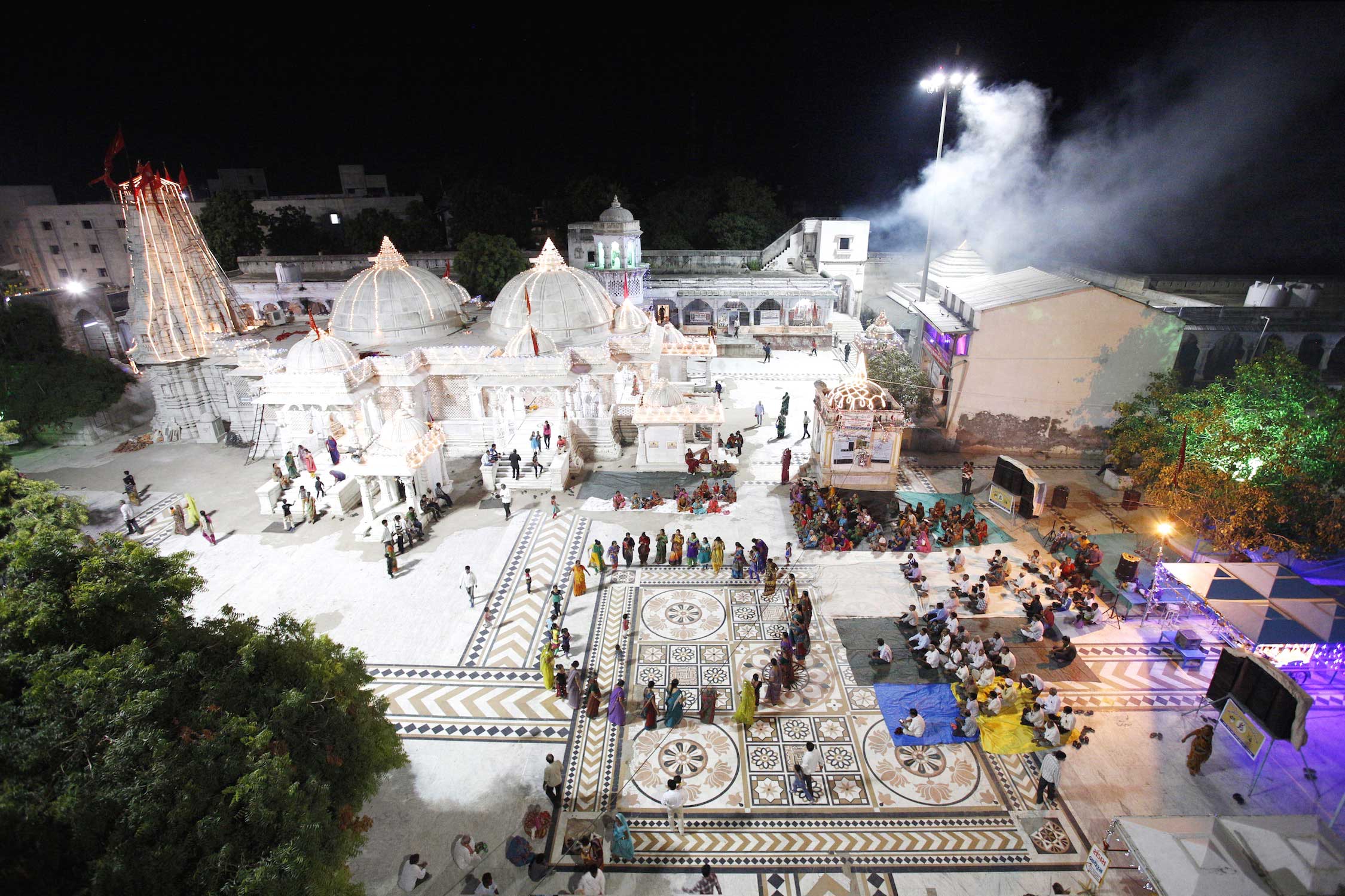 This temple in the north of Gujarat is entirely unknown. On the eighth day of Navratri,  women perform the ritual circle dance as the men are watching. In the background pilgrims are making offerings in the temple, that is decorated for the celebration with thousands of LED lights. On the upper right corner holy smoke fills the temple area, from a fire-temple in which Ayurvedic ingredients are burnt in a huge lot.
                              After long negotiations with the local priests, we were allowed to climb the temple roof  and gates, of this ancient temple. This temple and celebration has never been documented to this extend before.