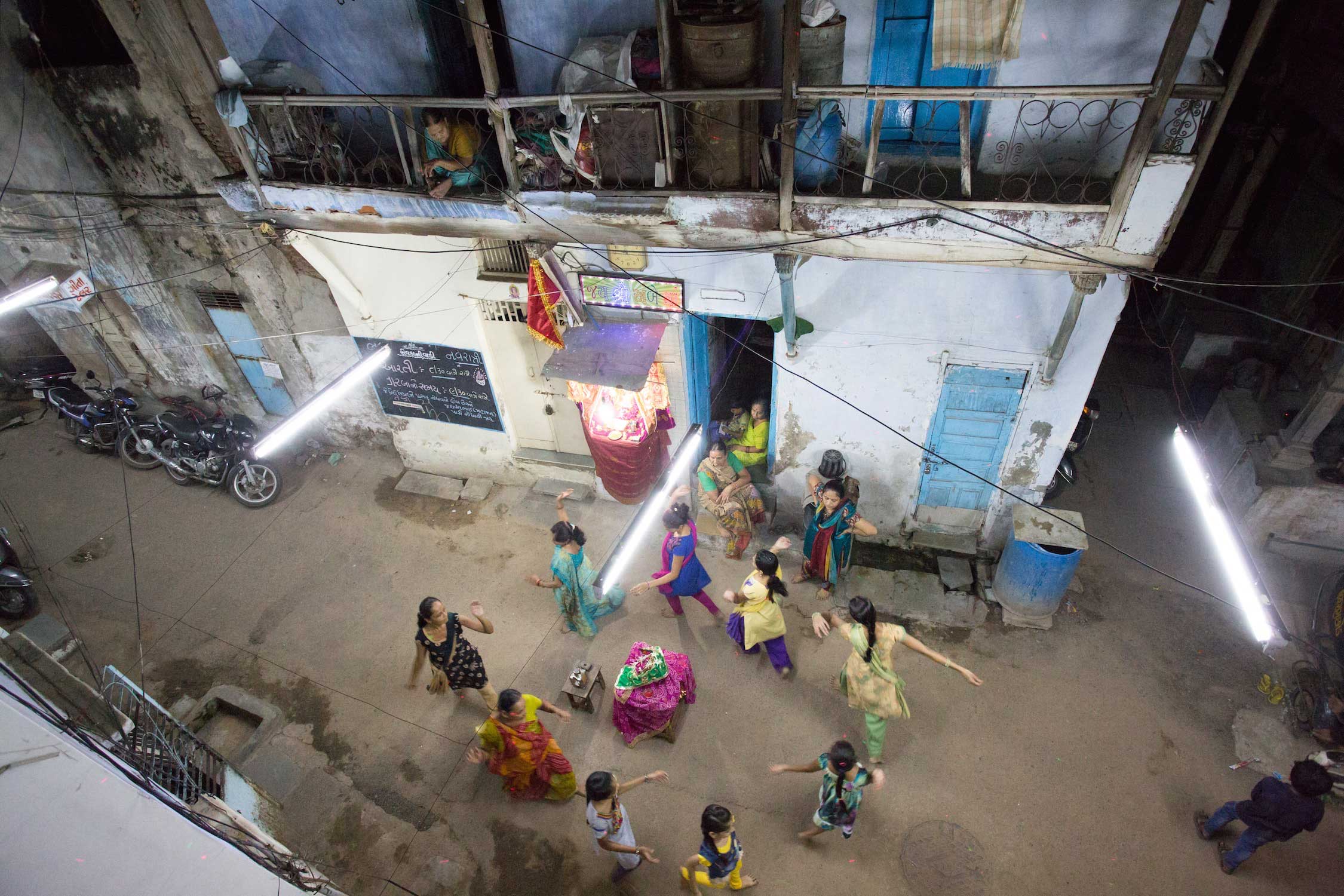 Old part of town in the capital of Gujarats. A family dances around the mother goddess figure and fire. Grandmothers watch the dance from the balcony and from inside.