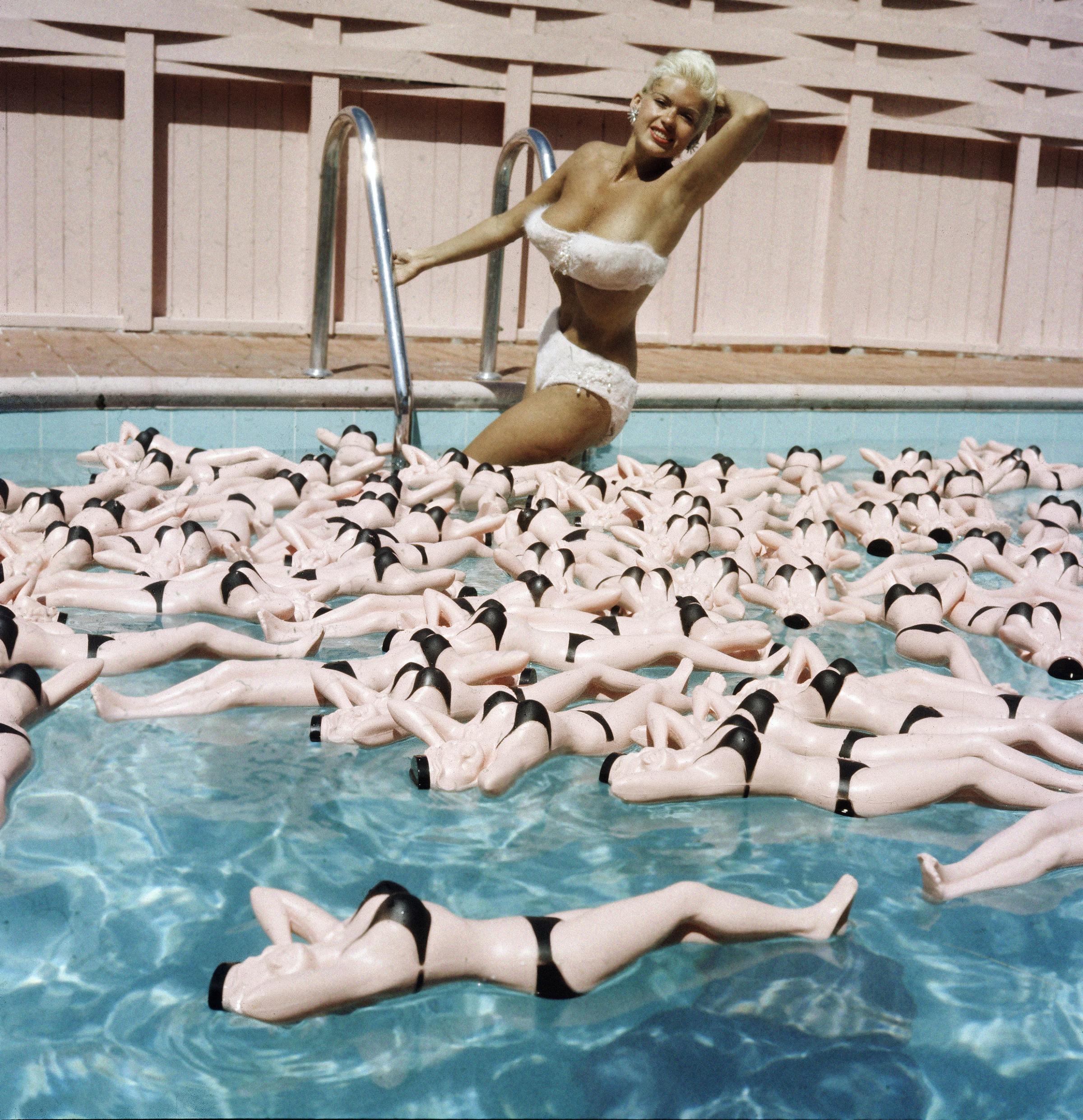 Jayne Mansfield posing hot water bottle likenesses floating around her in her pool.
