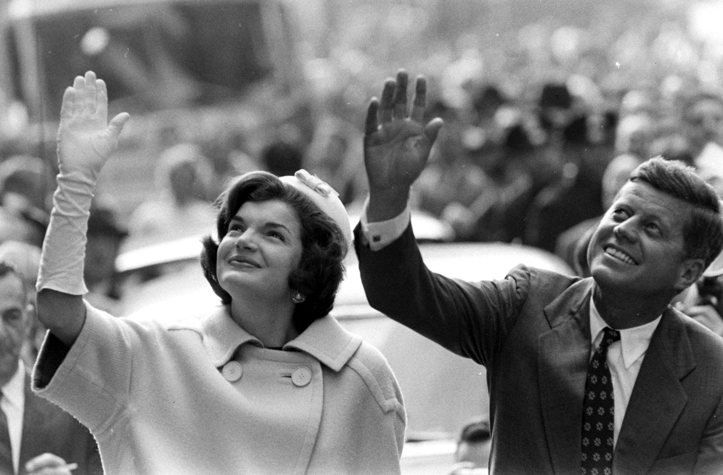 John F. Kennedy and wife Jackie waving to a crowd during campaign appearance.