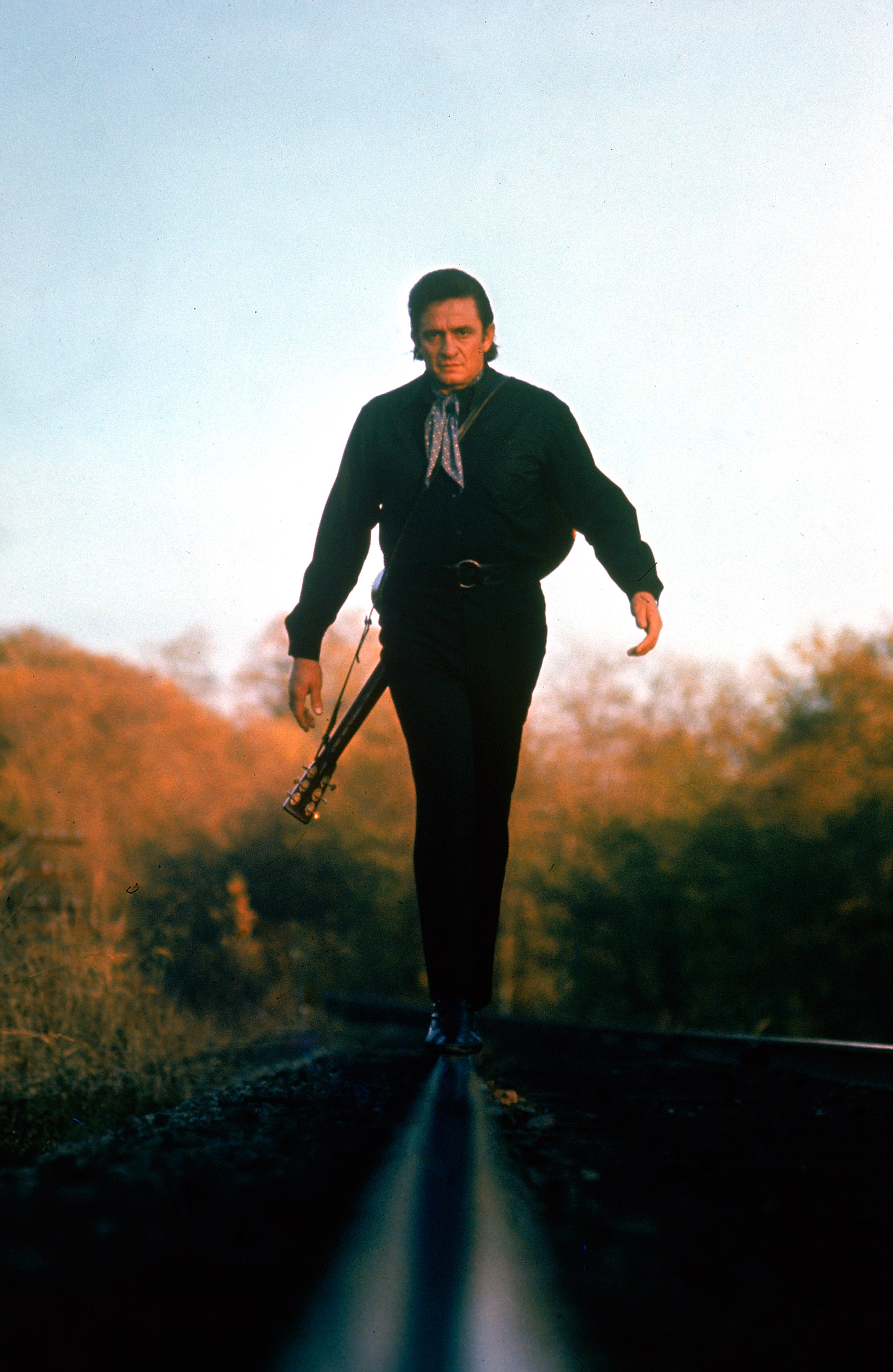Country music star Johnny Cash walking along the line of a railway track.