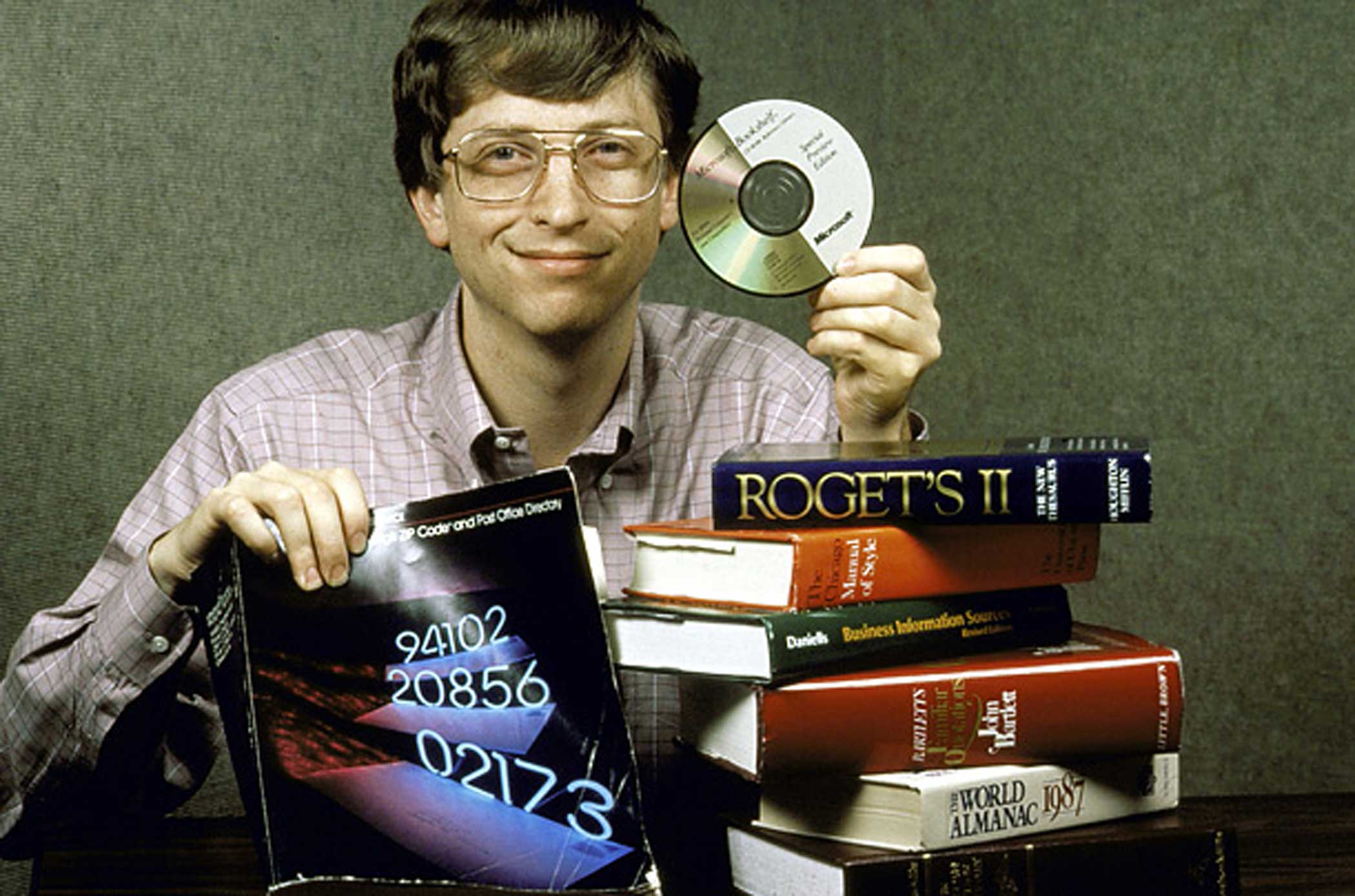 Microsoft Chairman Bill Gates, behind a pile of books, holds up Bookshelf, a new compact disc for computers which holds all the information contained in the books pictured.  (Photo by Doug Wilson//Time Life Pictures/Getty Images)