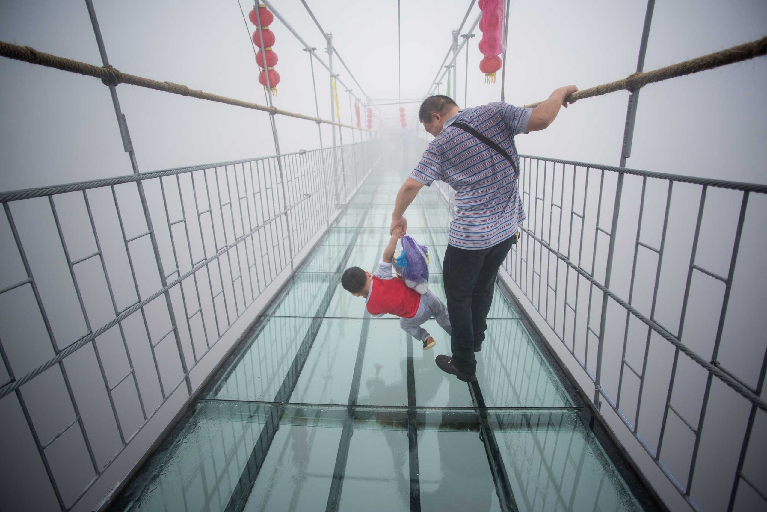 A Chinese tourist holds onto his son as they walk across a glass-bottomed suspension bridge in the Shinuizhai mountains in Pingjang county, Hunan province some 150 kilometers from Changsha on Oct. 7, 2015. (Johannes Eisele—AFP/Getty IMages)