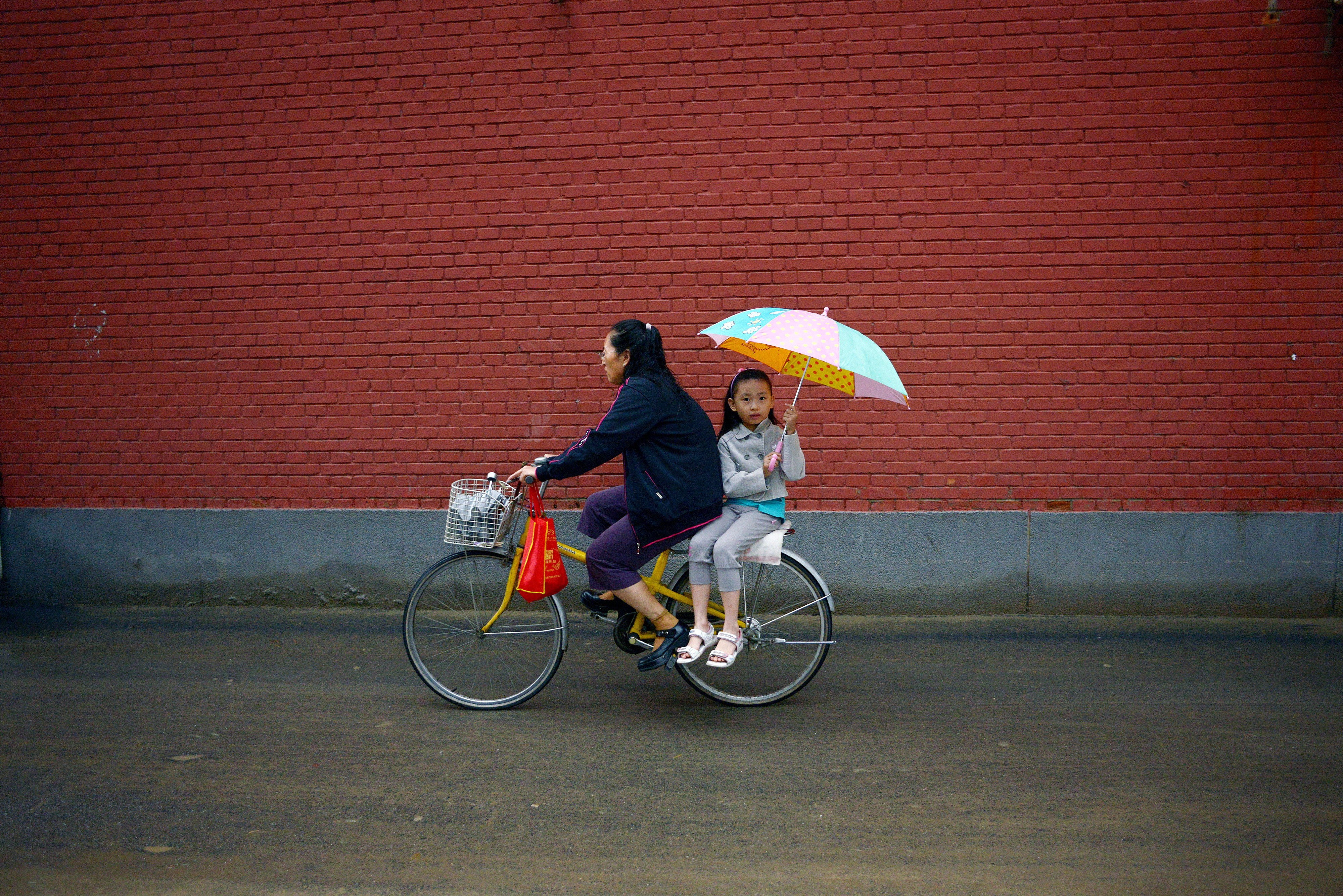 A girl holds an umbrella on the back of a bicycle along a road after school in Beijing on Sept. 2, 2014. (Wang Zhao—AFP/Getty Images)