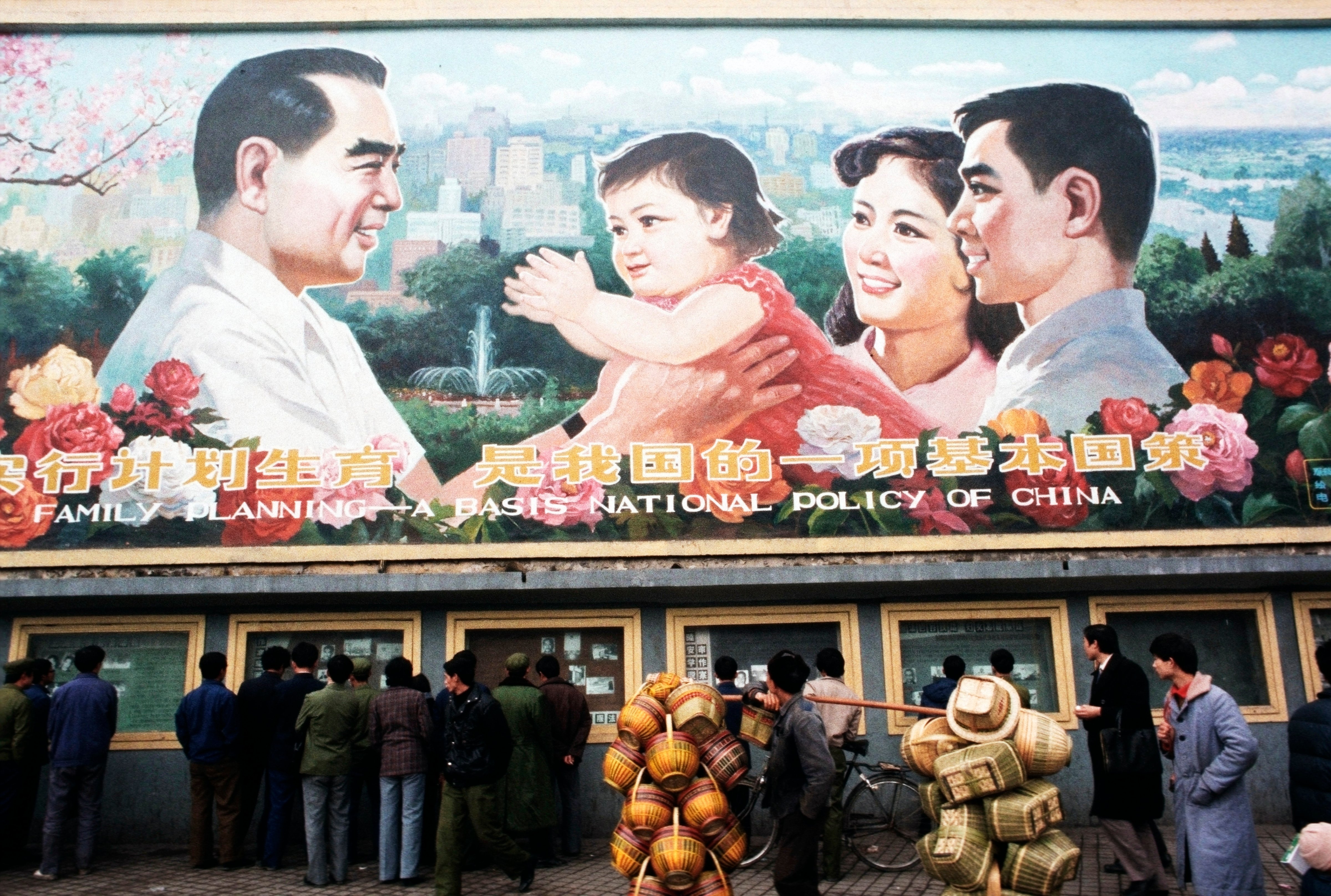 Pedestrians and a man carrying baskets pass by a huge billboard extolling the virtues of China's "One Child Family" policy. (Peter Charlesworth—Getty Images)