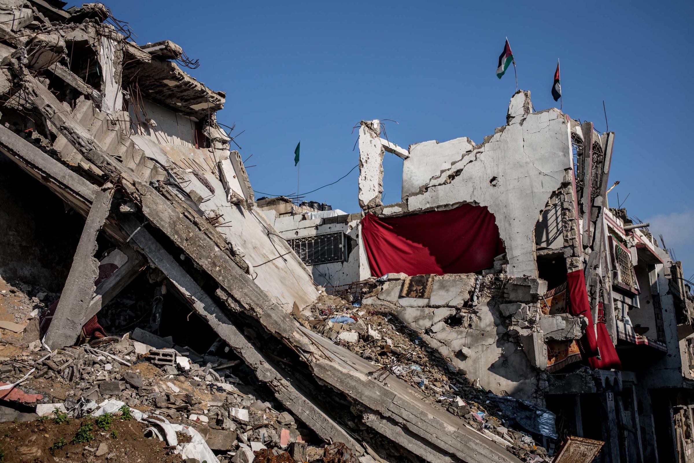In a partially destroyed building in Shejaiya, Gaza, red blankets are used to replace the missing walls. Two Palestinian flags and a Hamas one stand on the top of the building. Gaza Strip, December 2014.