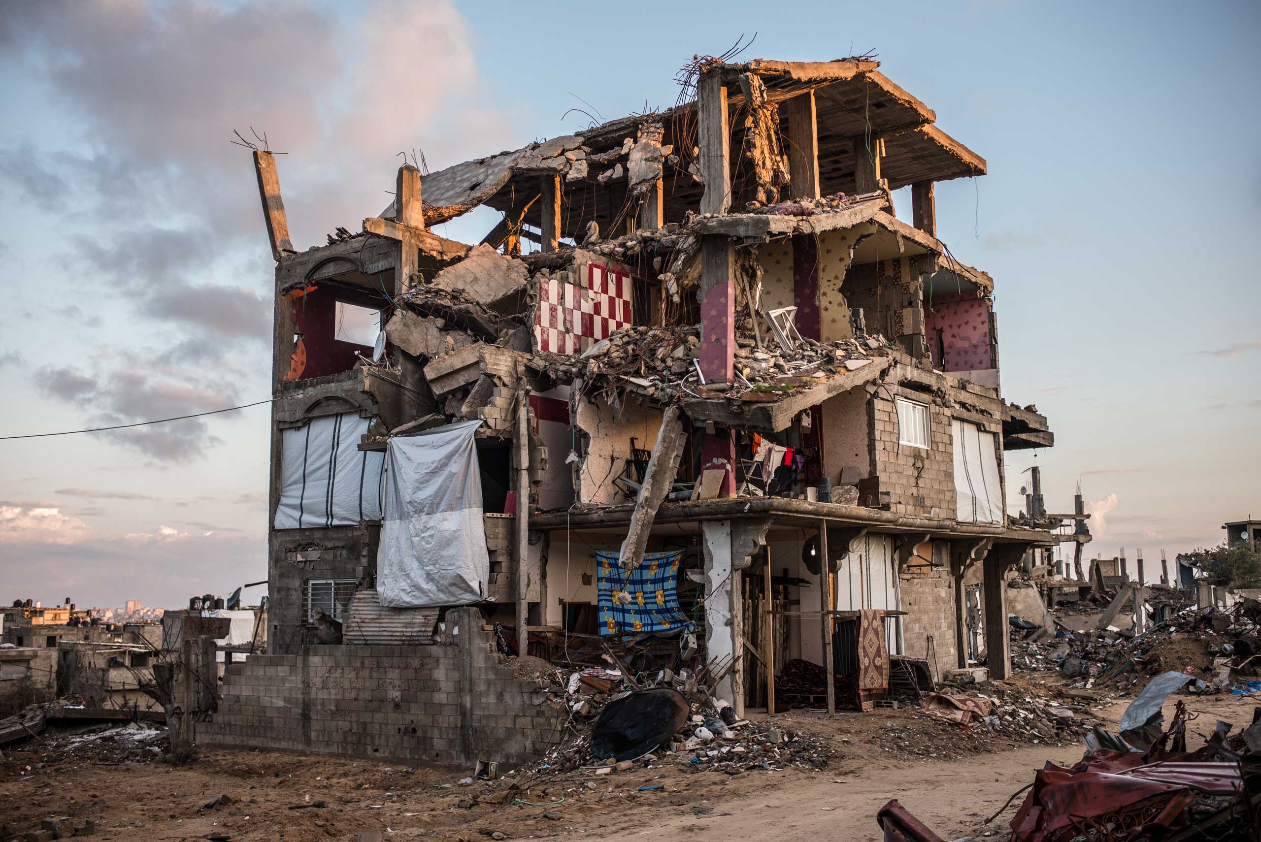 A partially destroyed building in Shejaiya, a neighborhood district of the Palestinian city of Gaza. Some family tried to replace the missing walls of their apartments with blankets. Shejaiya, the Gaza Strip. December 2014.