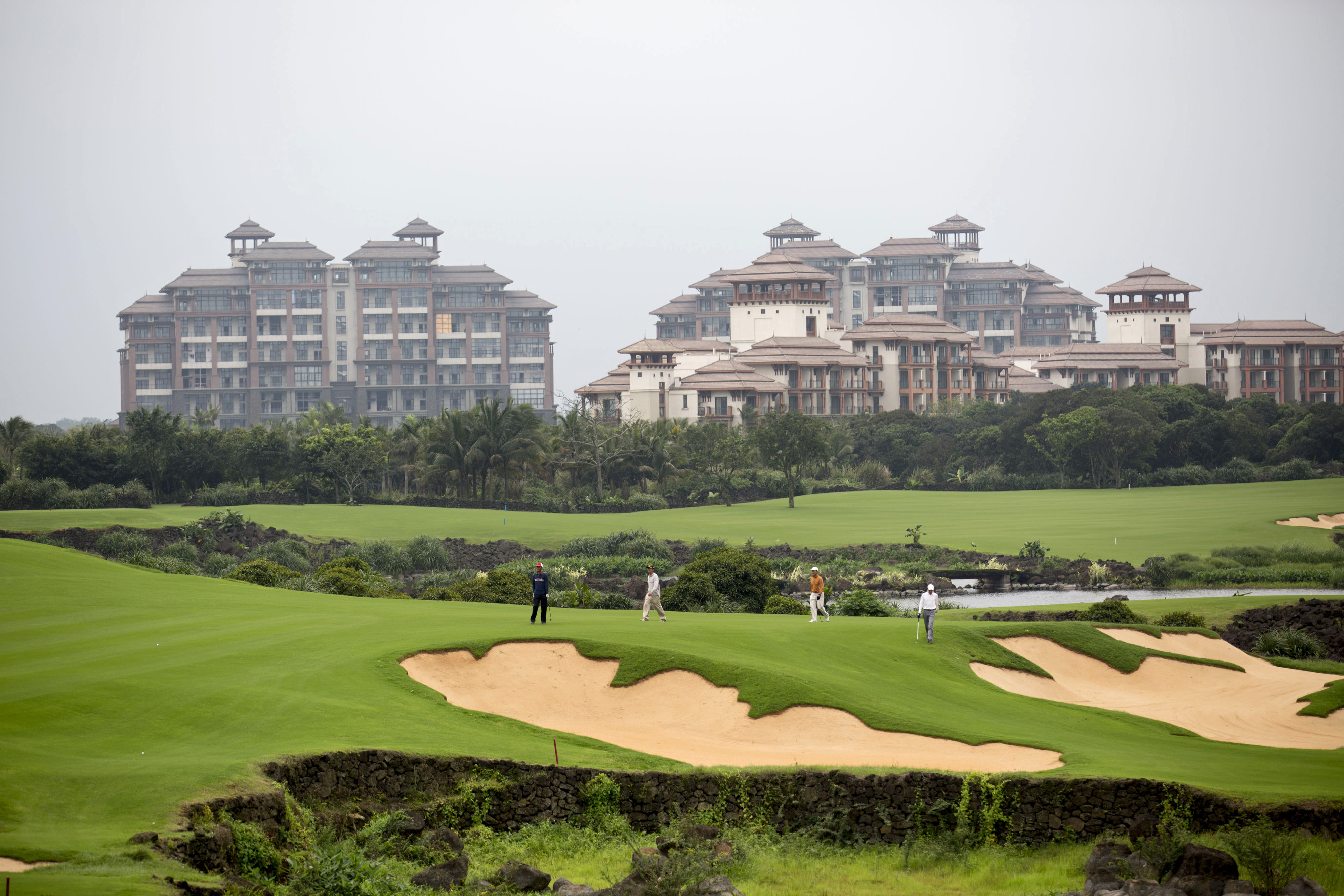 Residential properties stand in the background as men play golf at Mission Hills Resort Haikou in Haikou, in the Chinese province of Hainan province, on April 5, 2014 (Brent Lewin—Bloomberg/Getty Images)