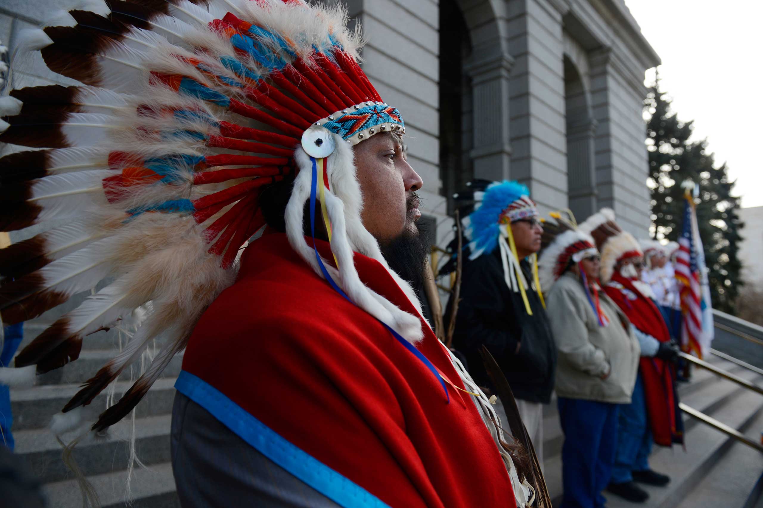 Native American Tribal member, Alan Fletcher, left, Cheyenne and Arapaho tribes, dons a traditional Native American headdress at the west steps of the Colorado Capitol, Dec. 03, 2014. (Andy Cross—Denver Post/Getty Images)