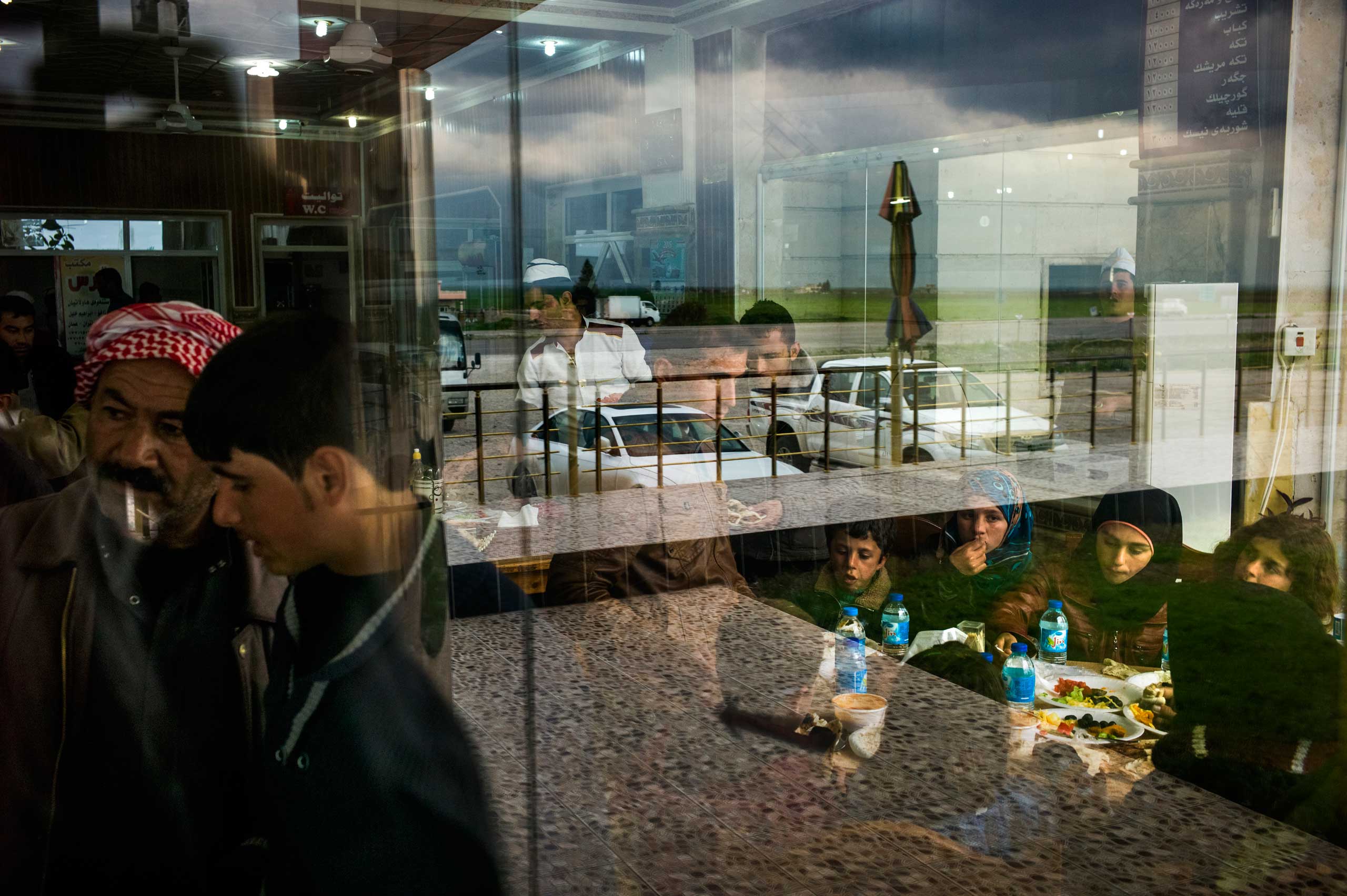 Nishan (centre) stays standing while he eats his lunch so that his sister-in-law and her children have a seat at the table in Amed Restaurant in Roviya. He and his family are traveling with over 300 other Syrian refugees from Kobani to the Gawilan Refugee camp in Iraq's Kurdistan. March 2015.