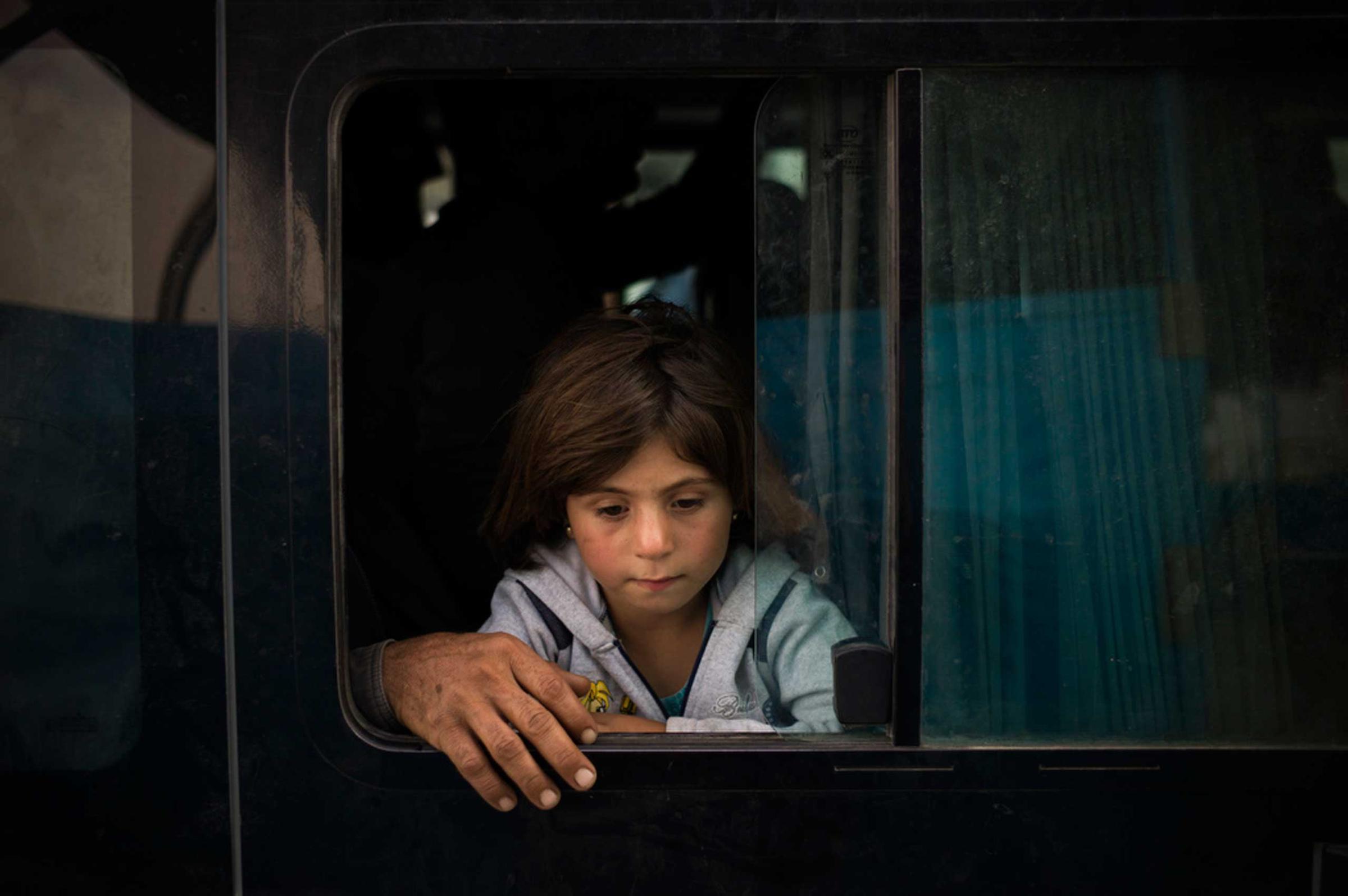 Iraq / Syrian Refugees / A young Syrian girl from Kobani and her fathers hand can be seen inside a bus arriving at a new transit point at the Ibrahim Khalil Border Crossing in Iraq after traveling by bus today from Turkey. Soon after arriving, they get moved to new buses which bring them to Gawilan Camp between Dohuk and Erbil. Most hope to leave the camp and look for work in major cities, many however will have to stay in camps around the Kurdish region. More then 2,000 Syrian refugee’s from Kobane have arrived since the Kurdish authorities in Iraq opened the border to Turkey on 10th October 2014 and the Kurdish authorities expect the numbers to rise to several tens of thousands in the coming days and weeks. / D. NAHR / October 2014