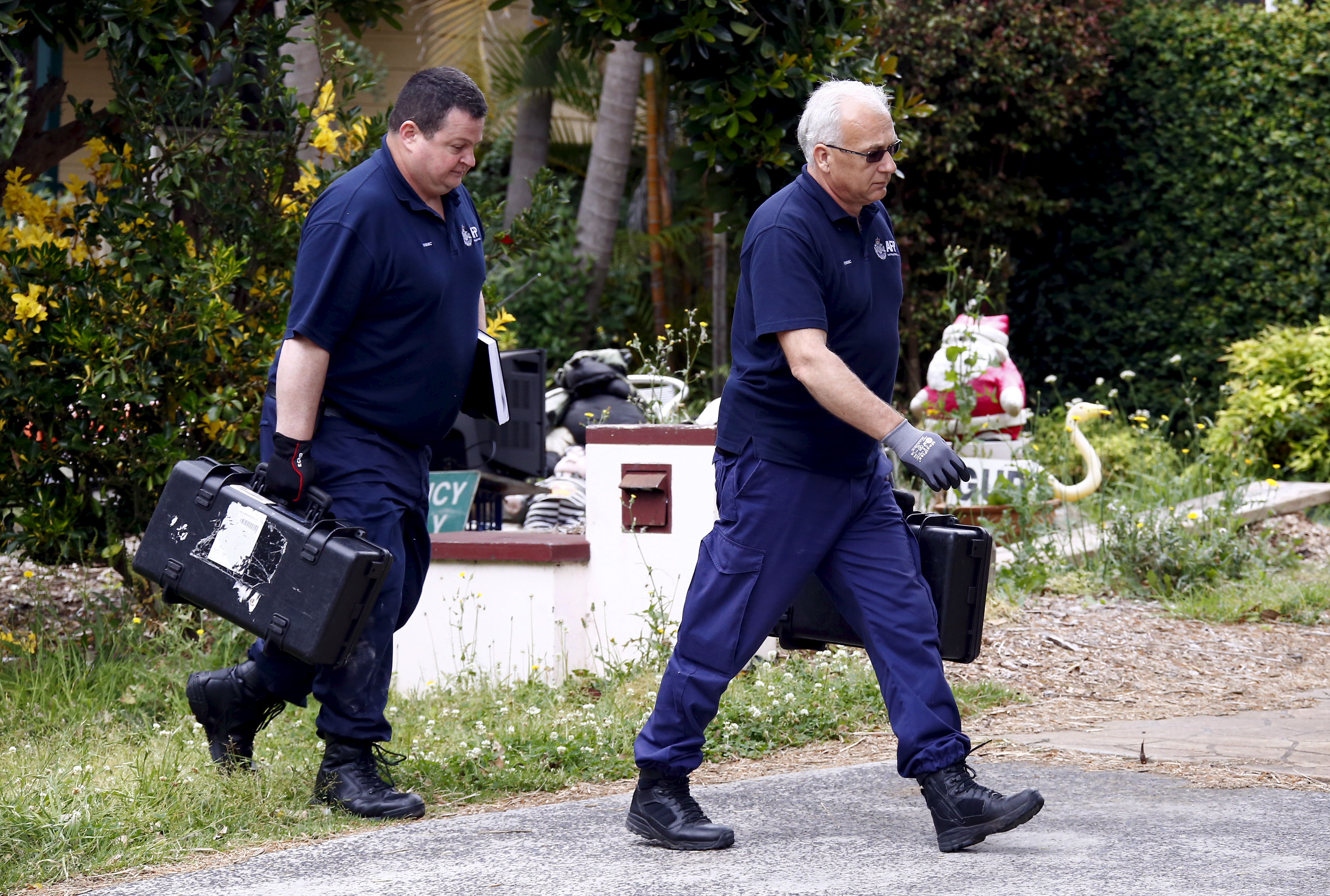 Federal police officers carry equipment into a house after arresting a man during early morning raids in western Sydney, Australia