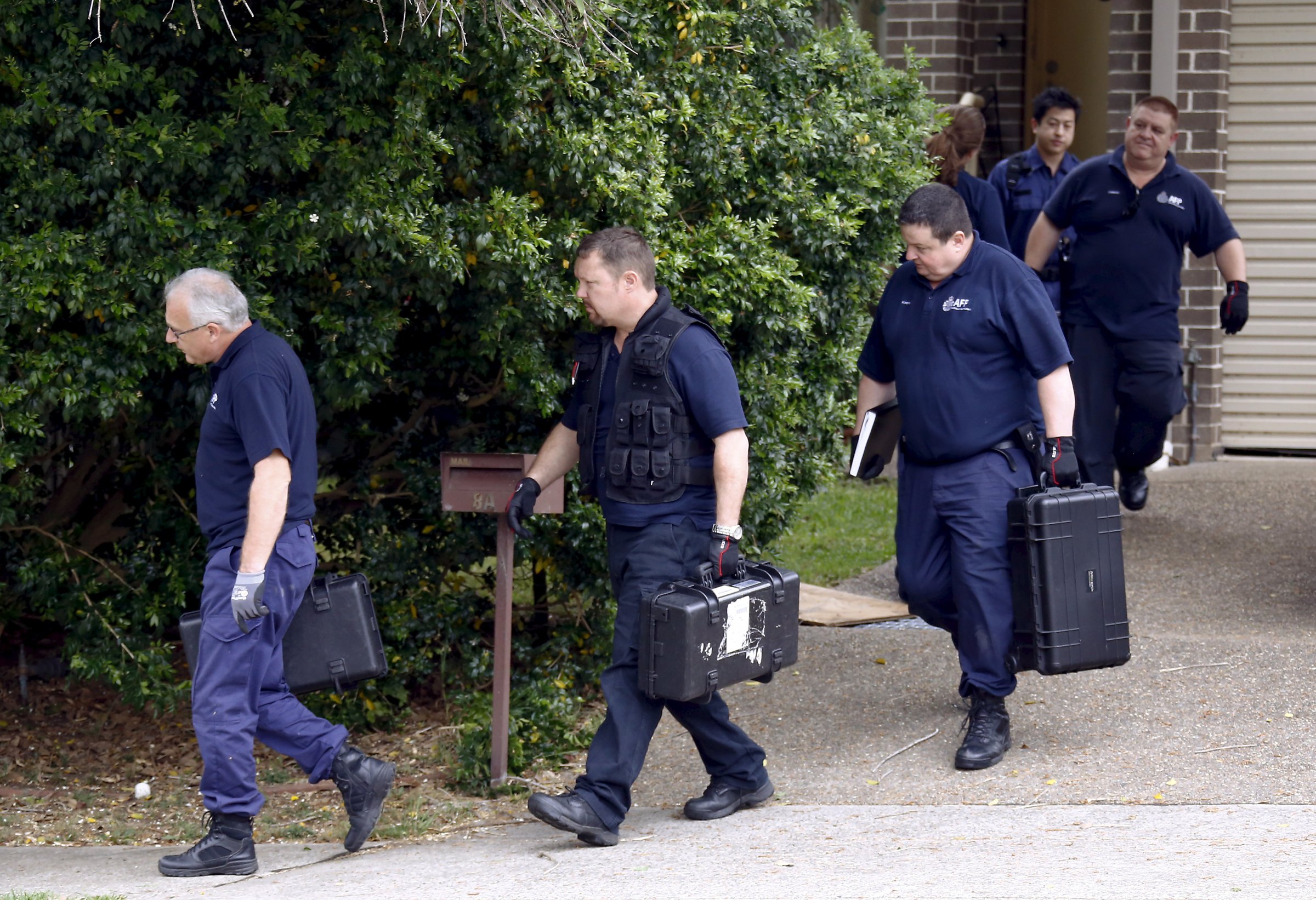 Australian Federal police officers carry equipment as they exit a house after arresting a man during early morning raids in western Sydney, Australia