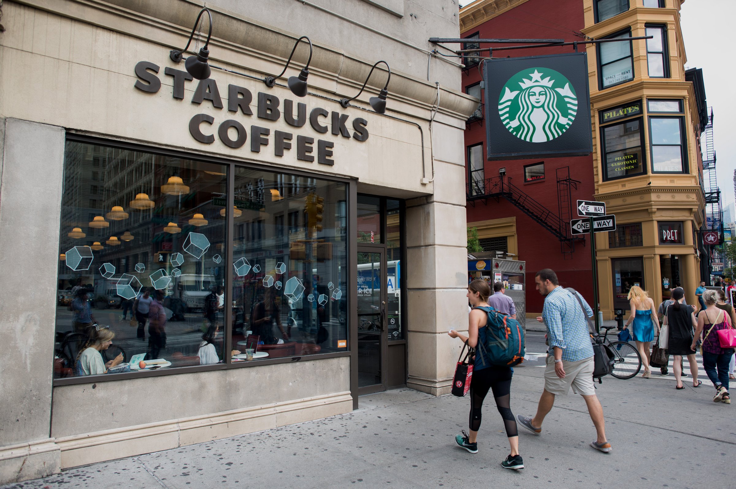 Pedestrians stroll by a Starbucks Coffee shop on the corner of Broadway and East 17th Street in Union Square in New York, New York, U.S., on Tuesday, July 21, 2015. Photographer: Craig Warga/Bloomberg *** Local Caption ***